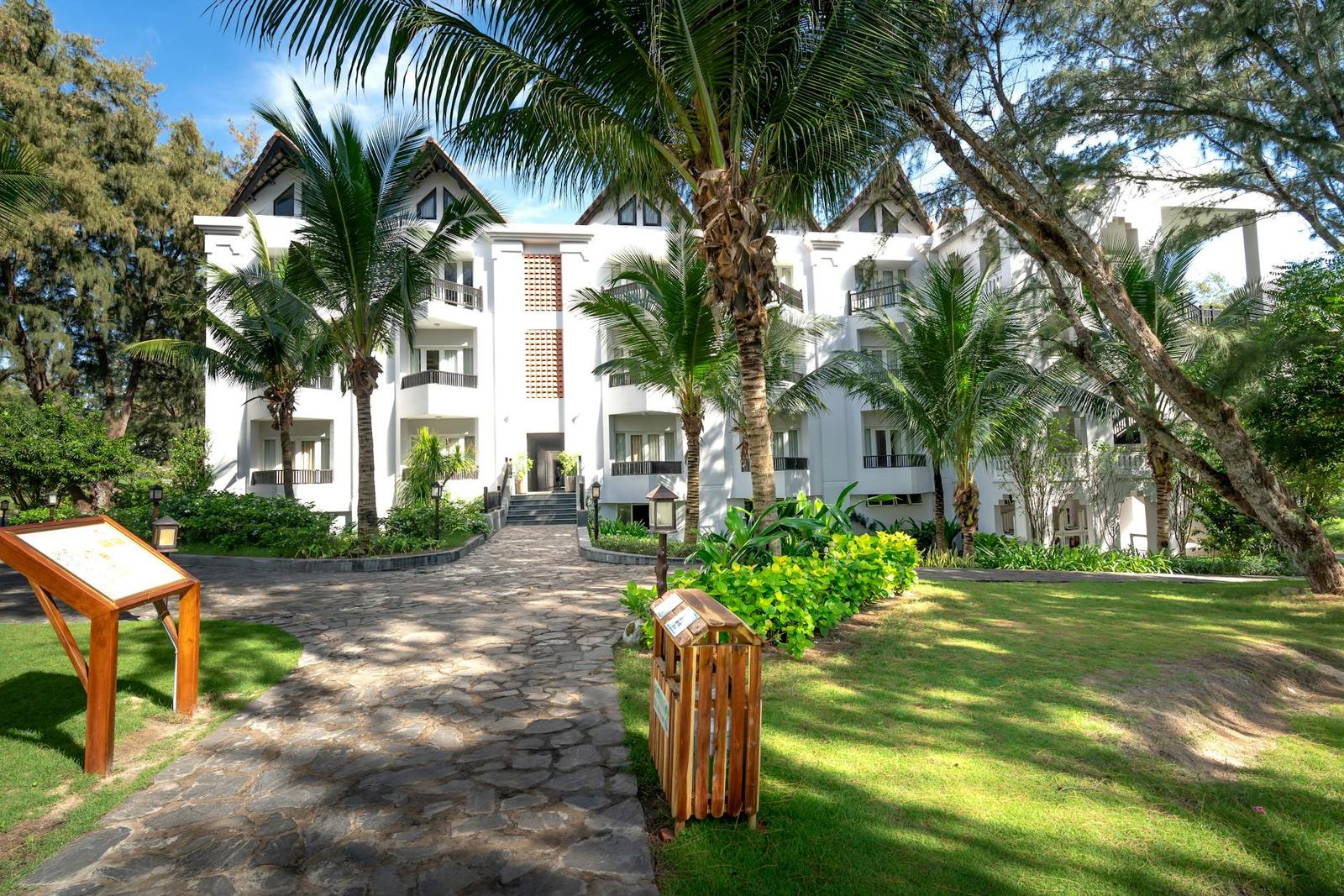 A white multi-storey resort building framed by tall palm trees along a stone path