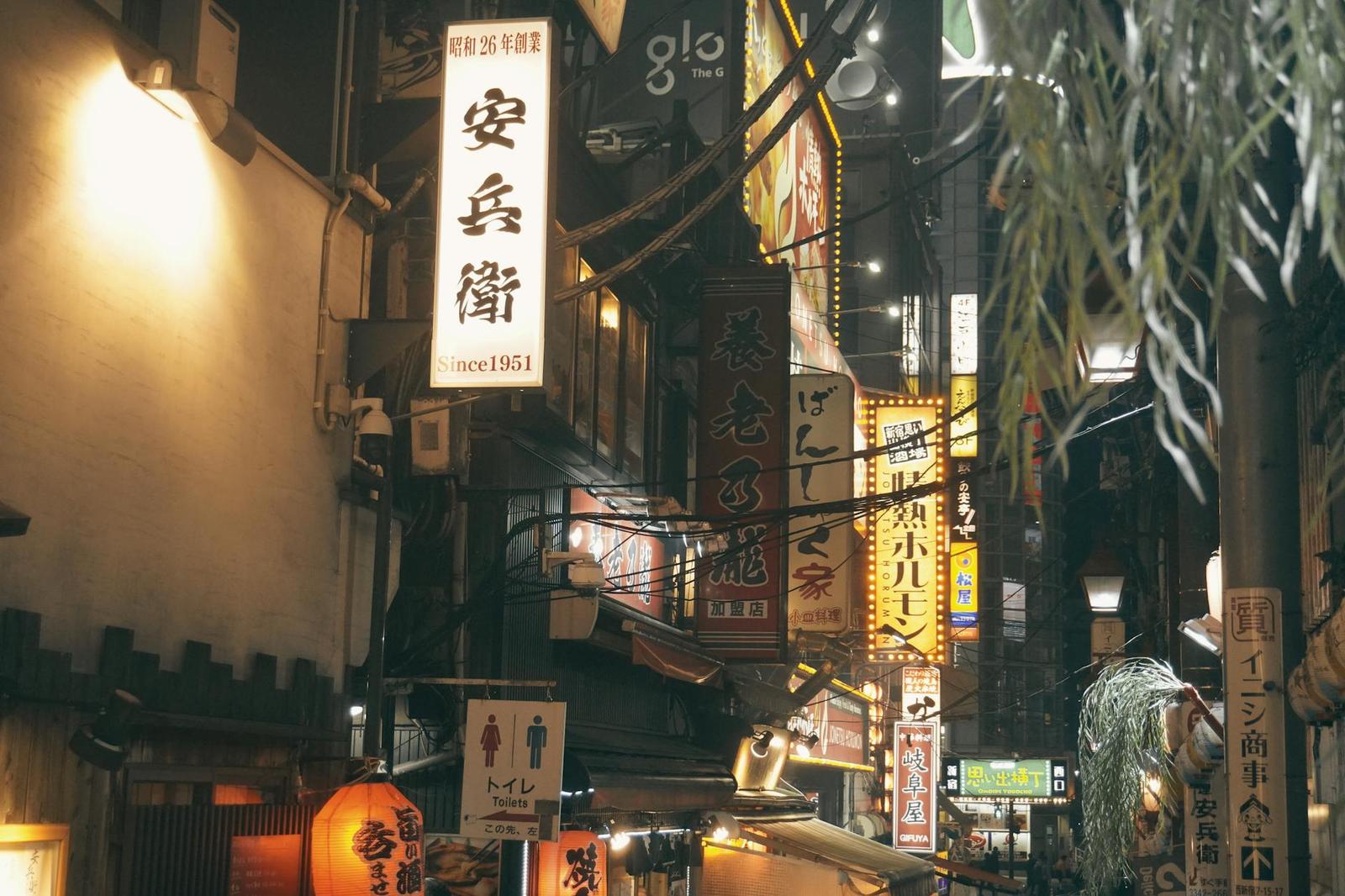 An alley of illuminated shop signs and lanterns at night