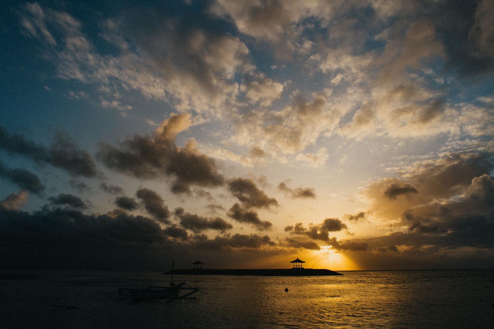 A golden sunset over water with a silhouetted temple gate on the horizon