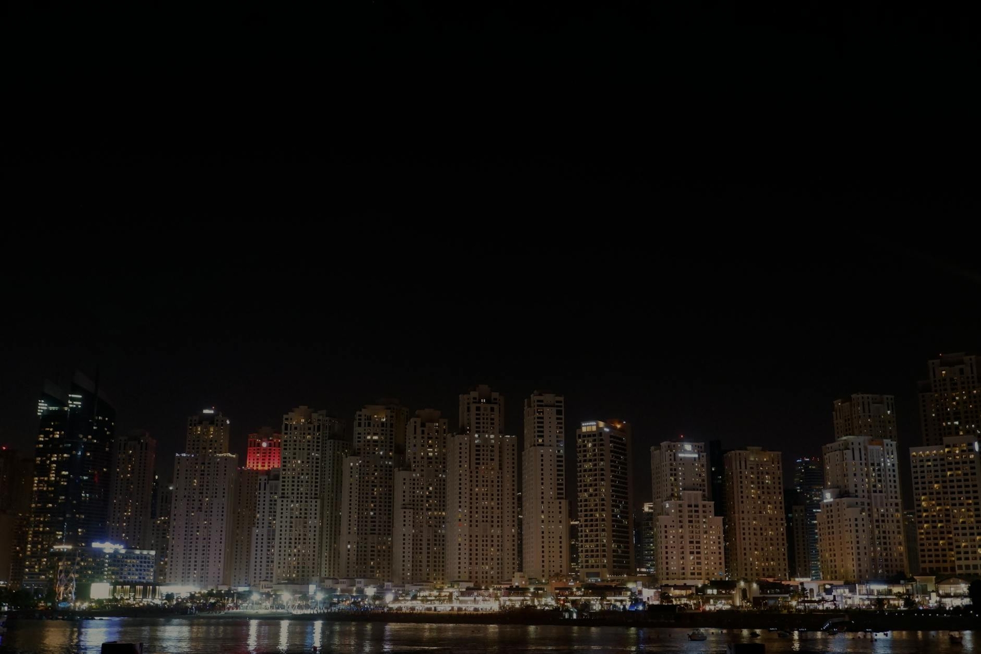 A dark city skyline of lit towers along the waterfront at night