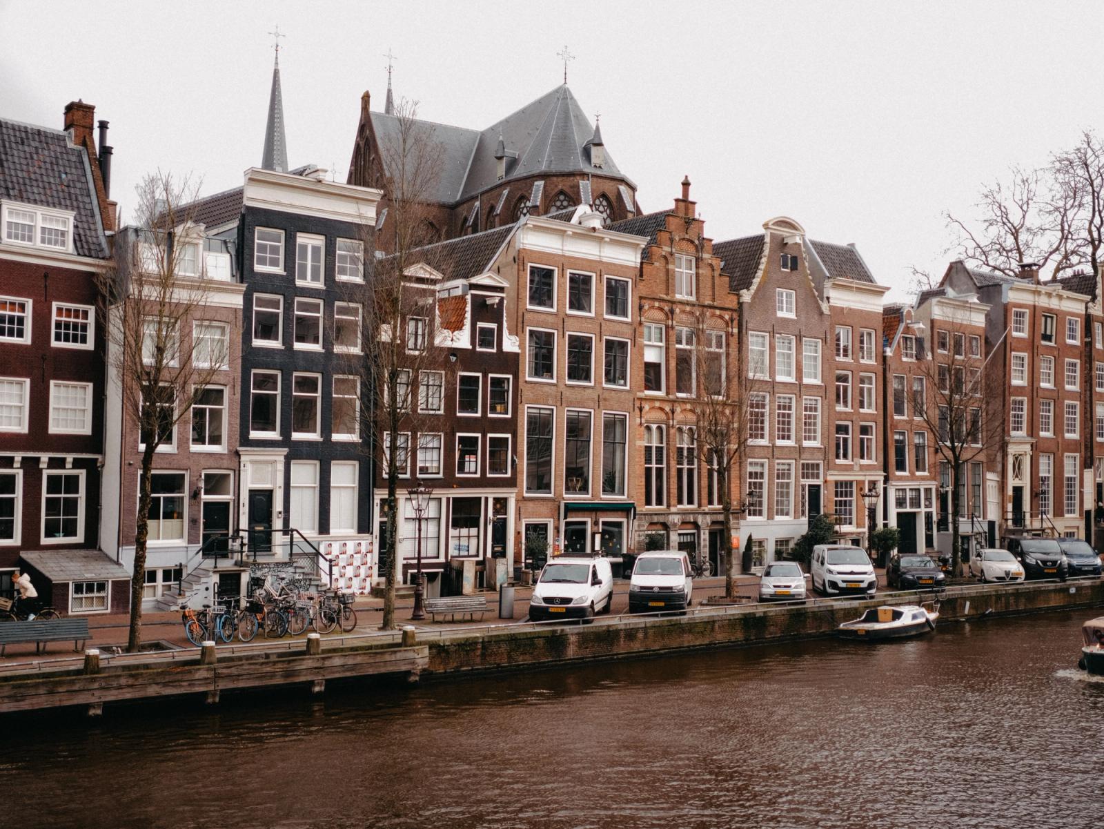 Scenic view of Amsterdam's iconic canal and traditional Dutch row houses with canal boats and cars lined up