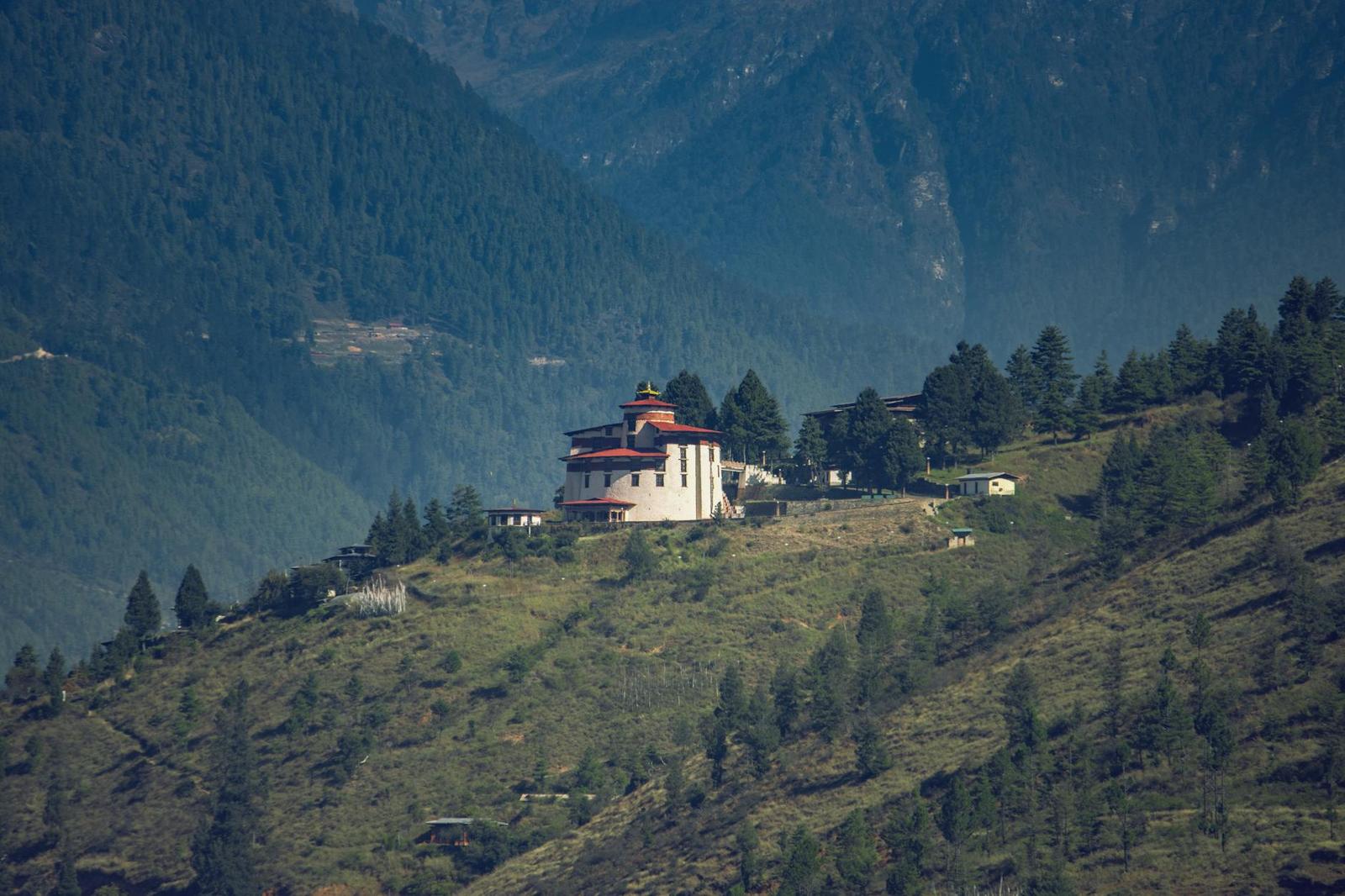 A white monastery building perched on a forested hilltop