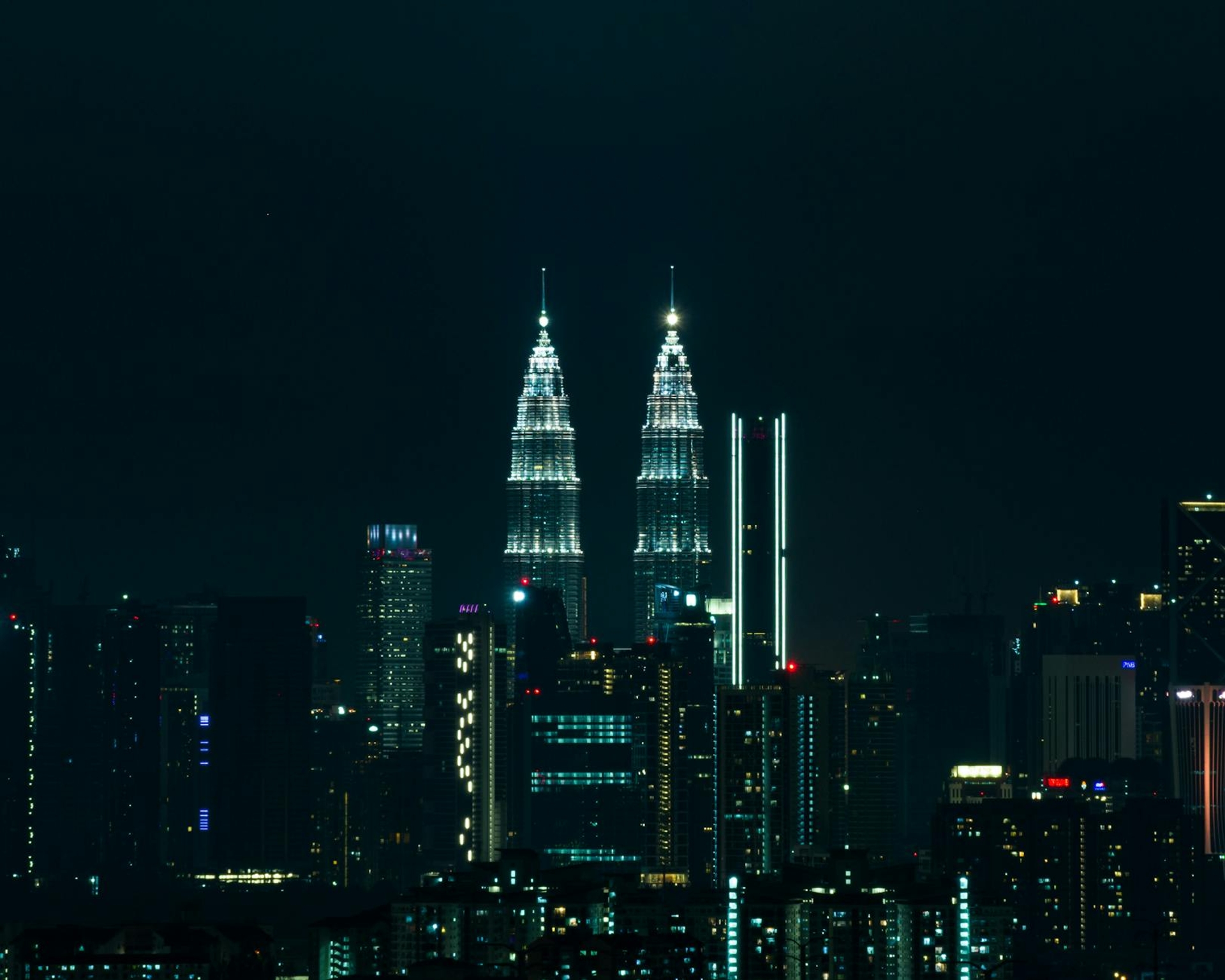 A city skyline with twin illuminated towers rising above dark buildings at night