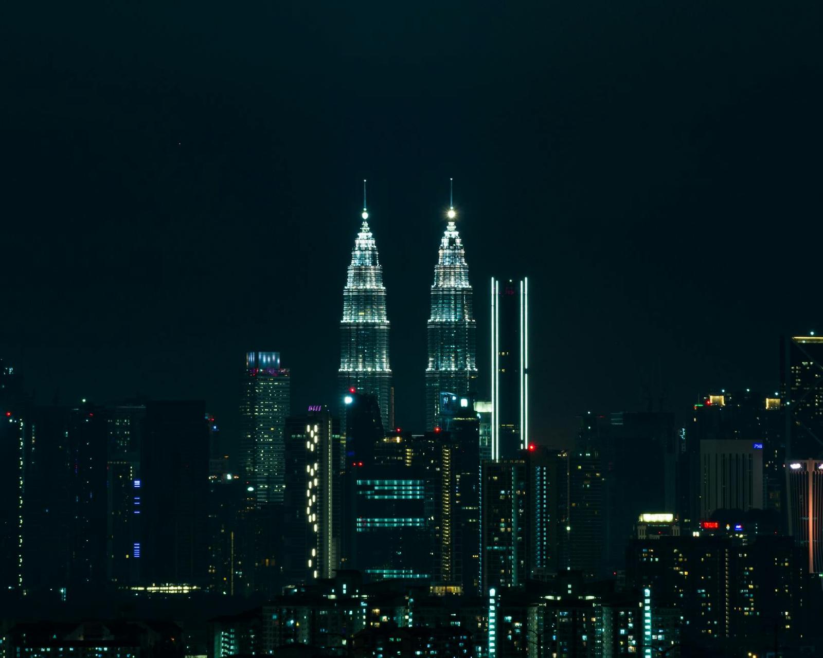 A city skyline with twin illuminated towers rising above dark buildings at night