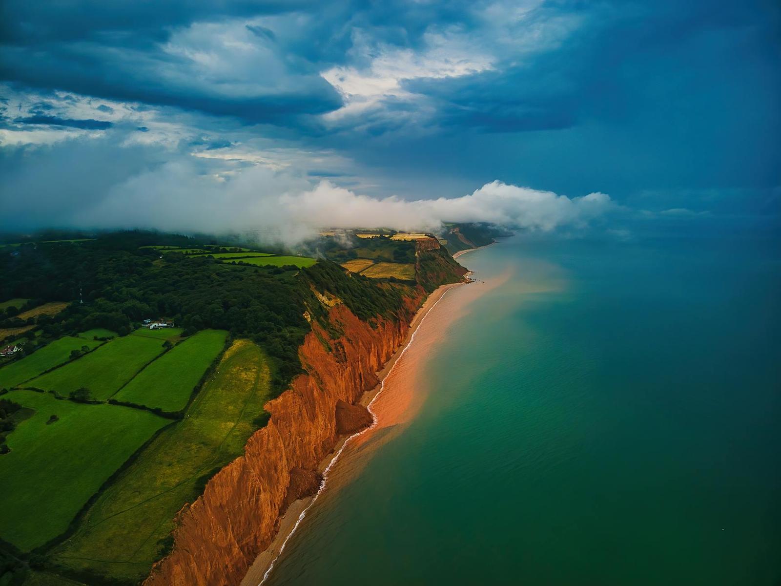 Storm clouds rolling over red cliffs and green farmland along a coastline