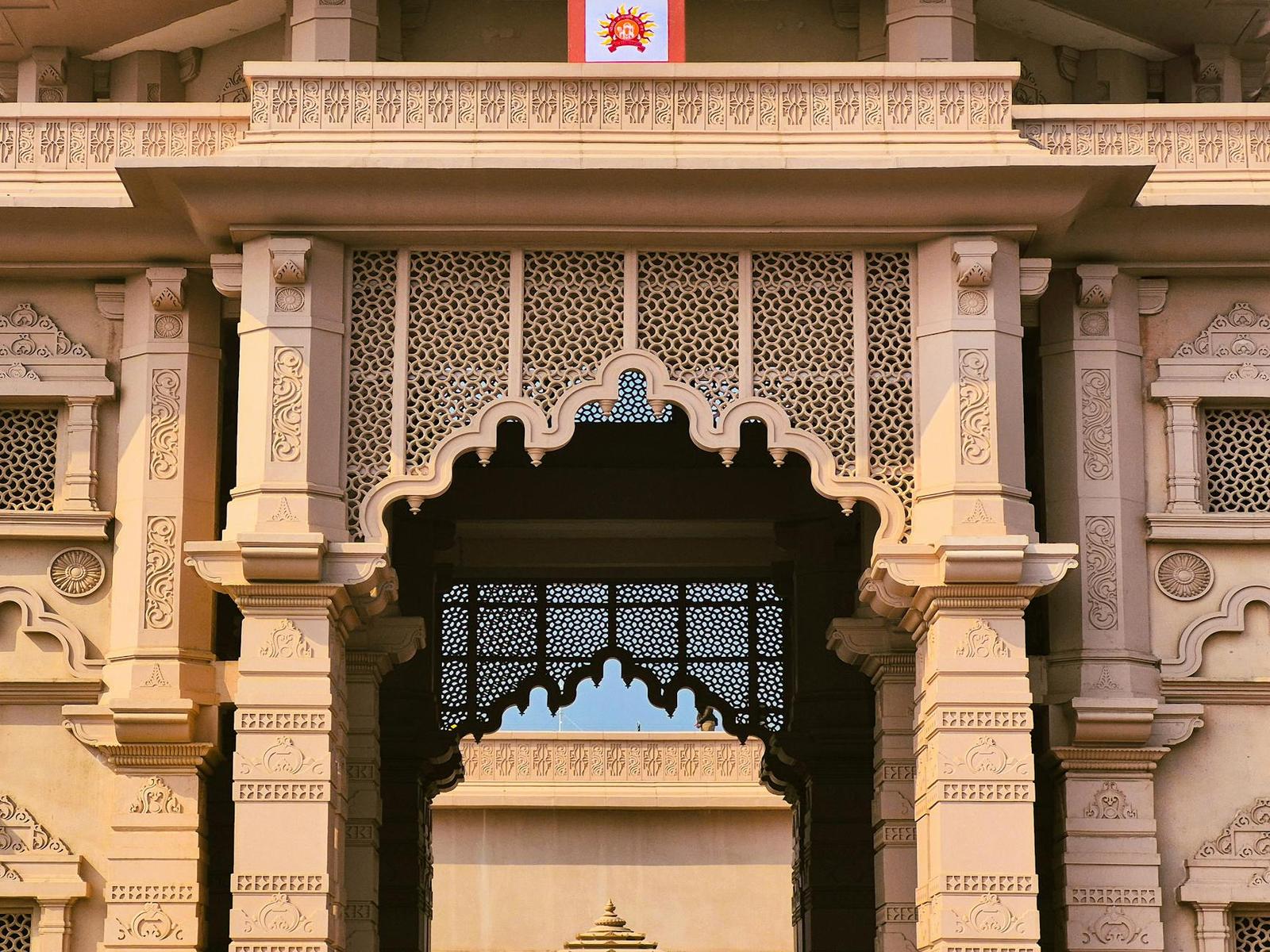 An ornate carved sandstone archway with a lattice window above a temple entrance