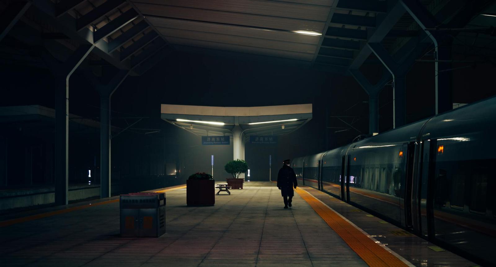 A lone traveller walking along a dim railway platform at night beside a train