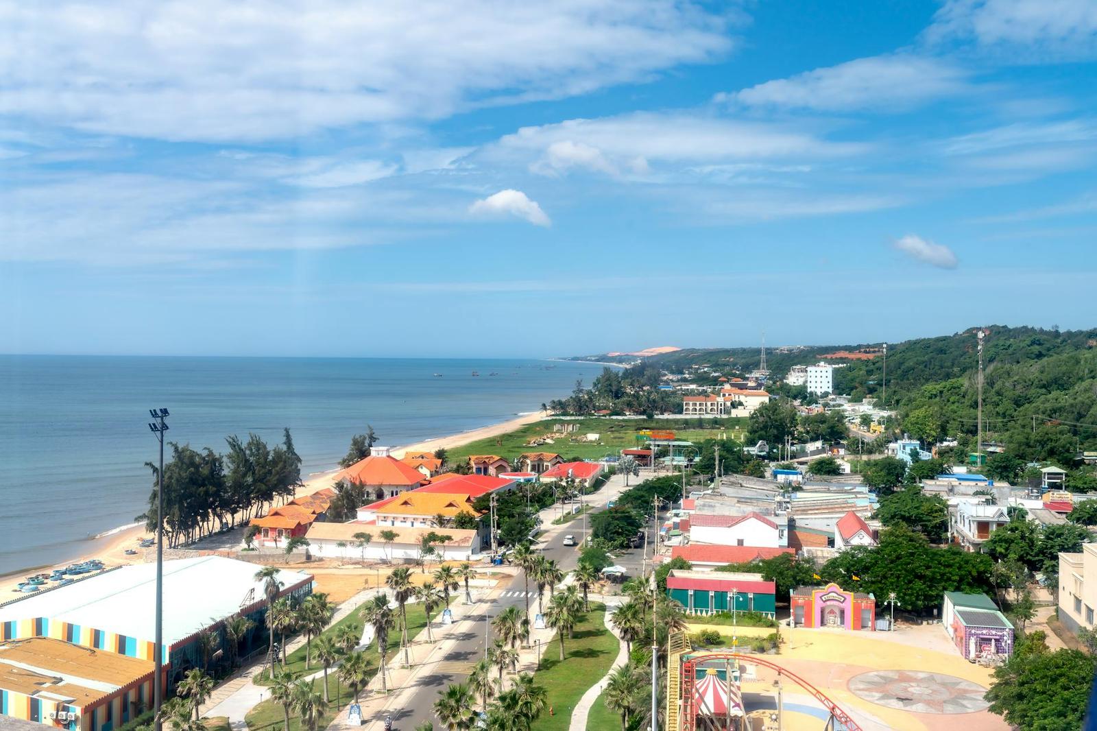 Aerial view of a coastal town with a palm-lined promenade beside a sandy beach