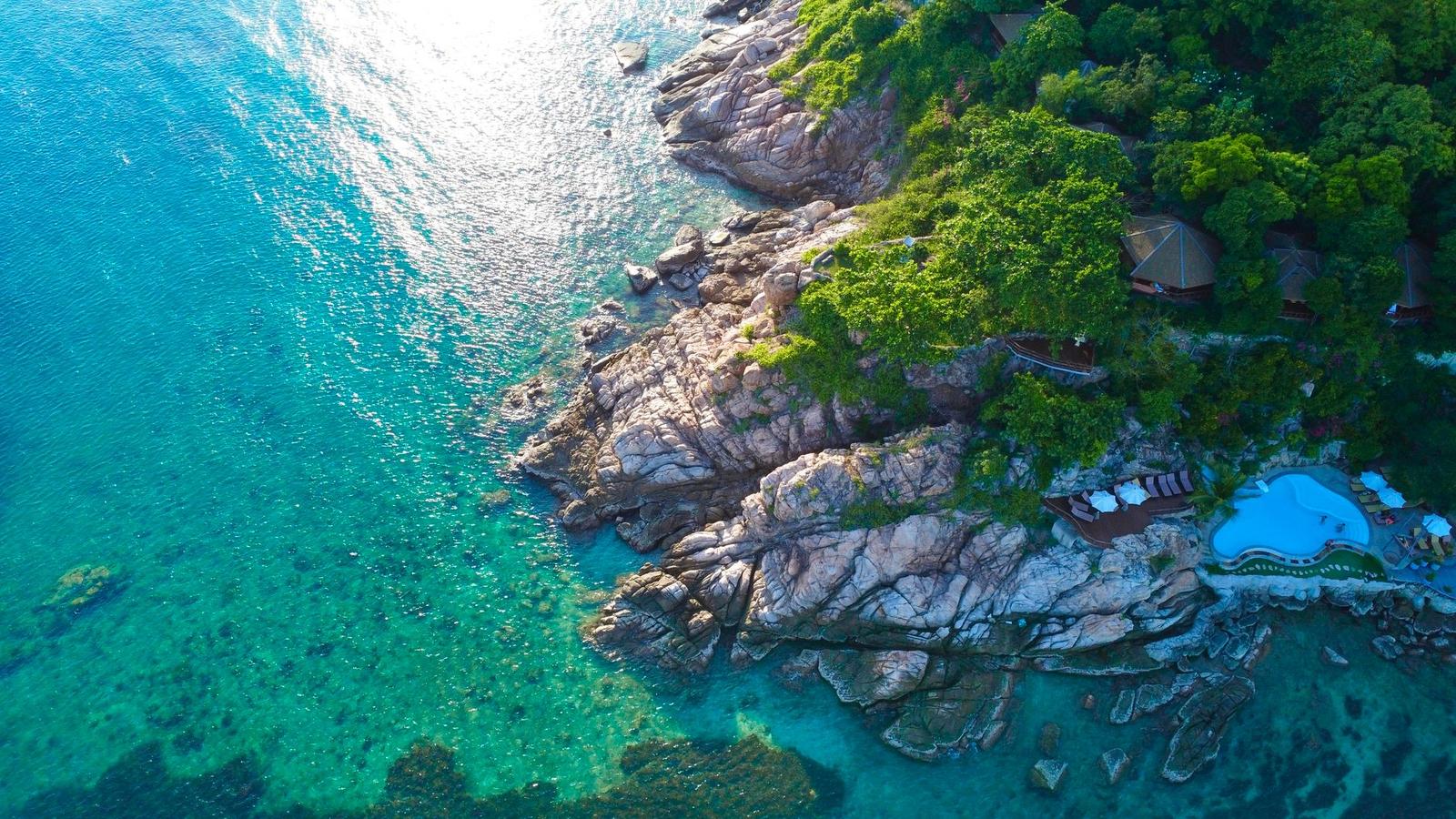 Aerial view of a rocky cove with a resort pool set among boulders and trees