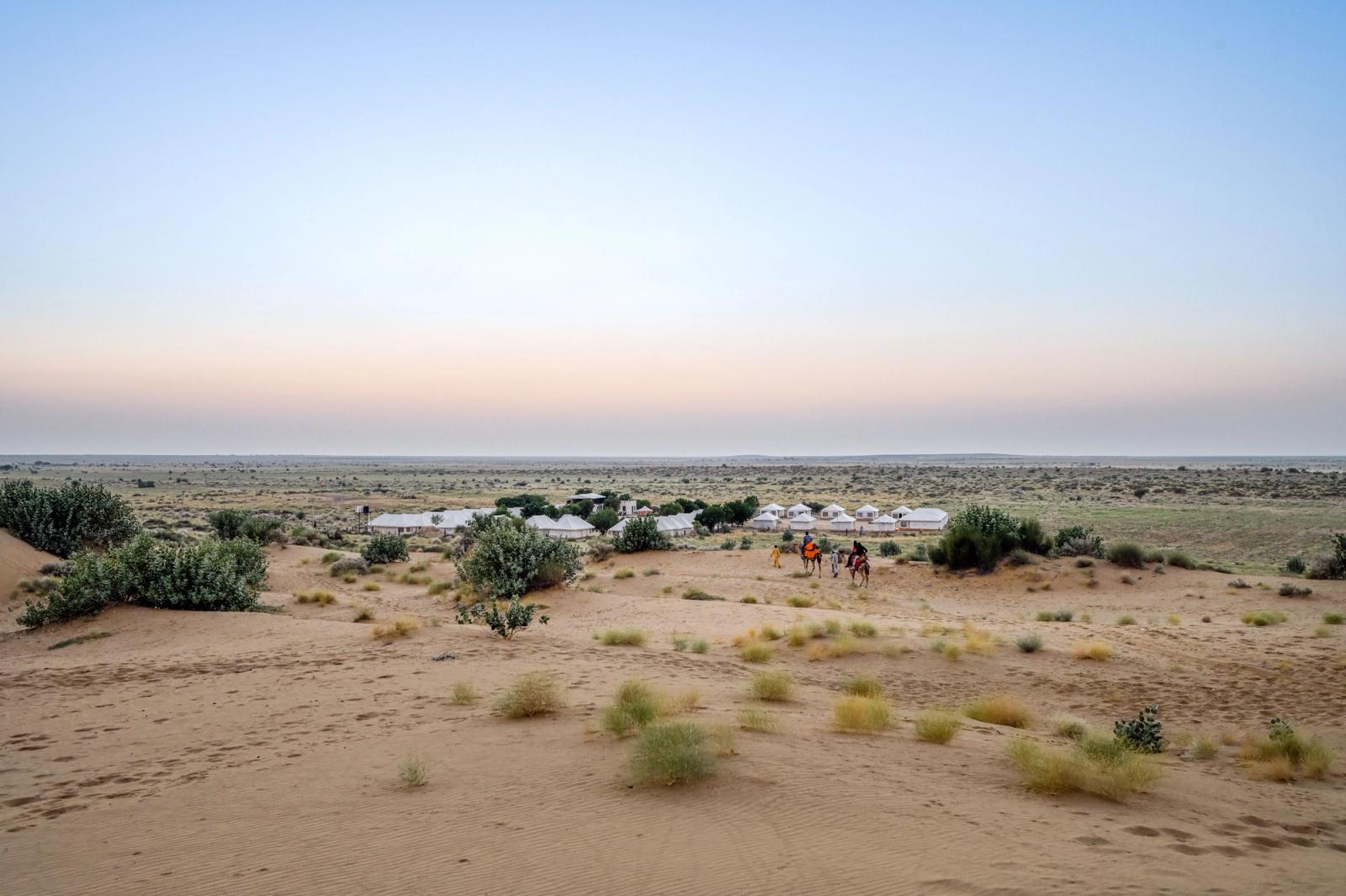 Aerial view of a desert camp of white tents among dunes at dusk