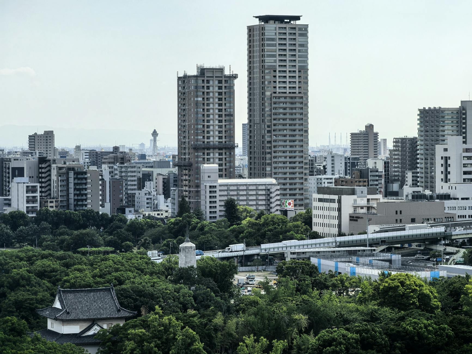 High-rise towers and a monorail line above a park with a traditional gate