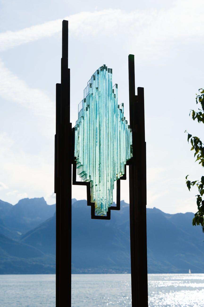 Glass sculpture on metal posts silhouetted against a lakeside mountain view