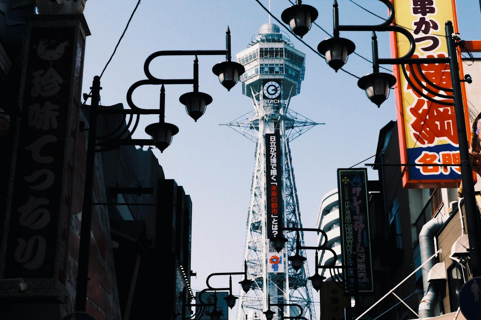 A slender observation tower rising above a street strung with lanterns and signs