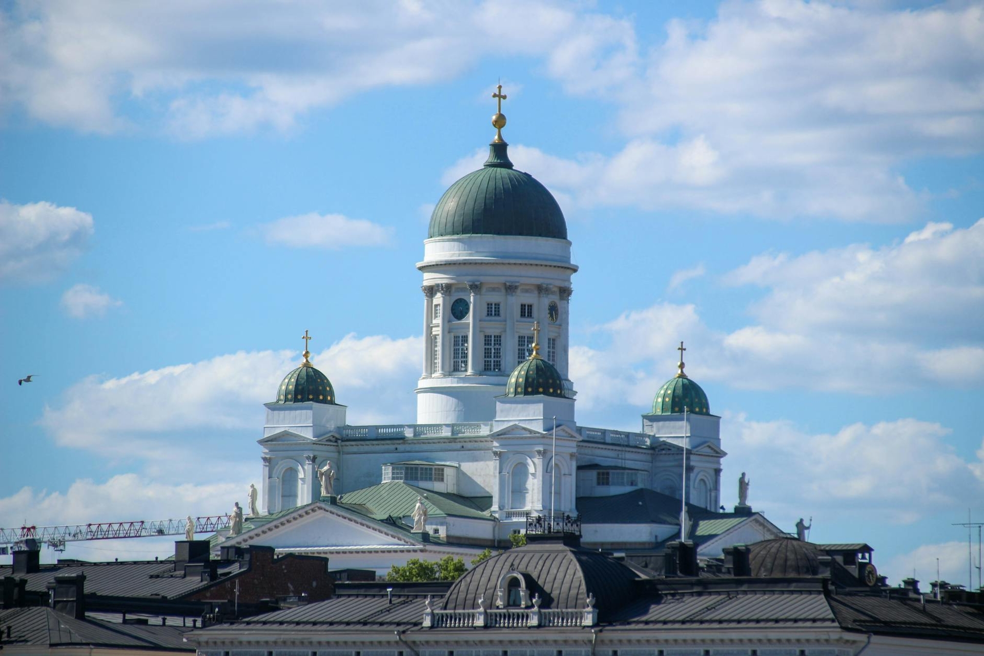 A stunning view of Helsinki Cathedral with its green domes and cross, under a bright blue sky