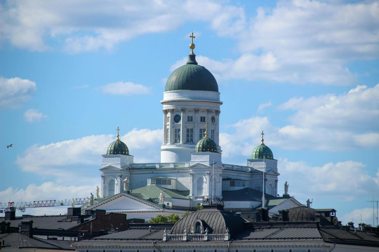 A stunning view of Helsinki Cathedral with its green domes and cross, under a bright blue sky