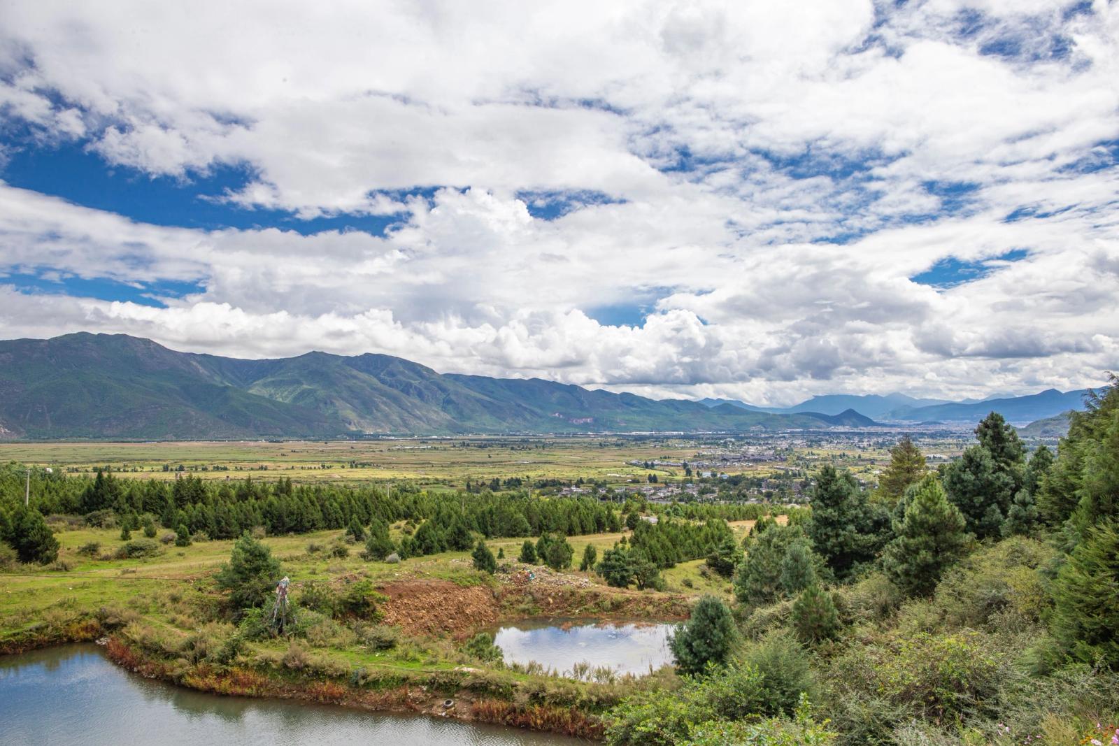 Panoramic view of a picturesque mountain valley with scattered clouds and lush greenery, perfect for travel inspiration