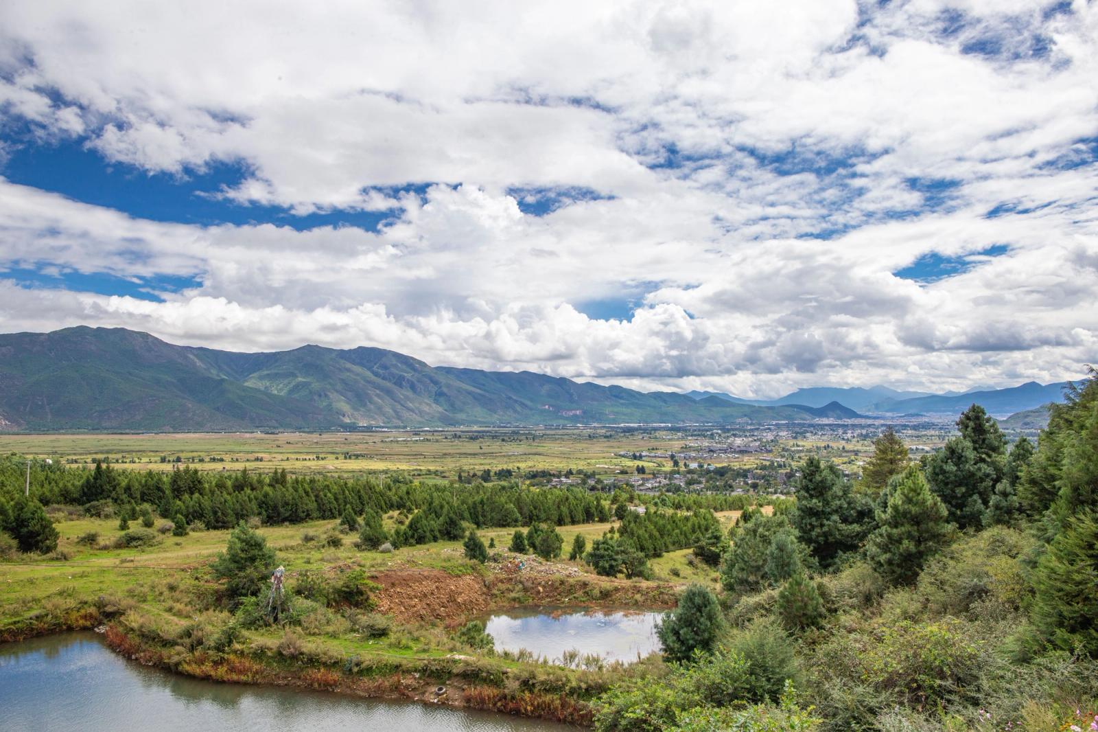 Panoramic view of a picturesque mountain valley with scattered clouds and lush greenery, perfect for travel inspiration