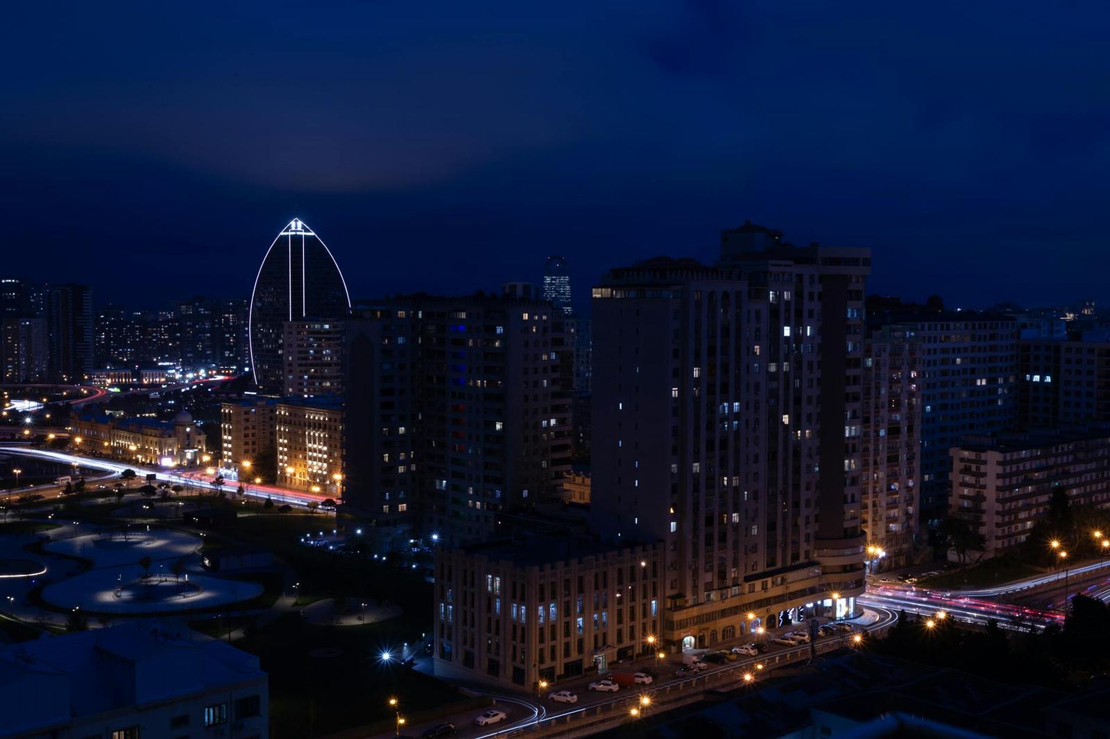 City apartment towers glow at night beside an oval illuminated structure