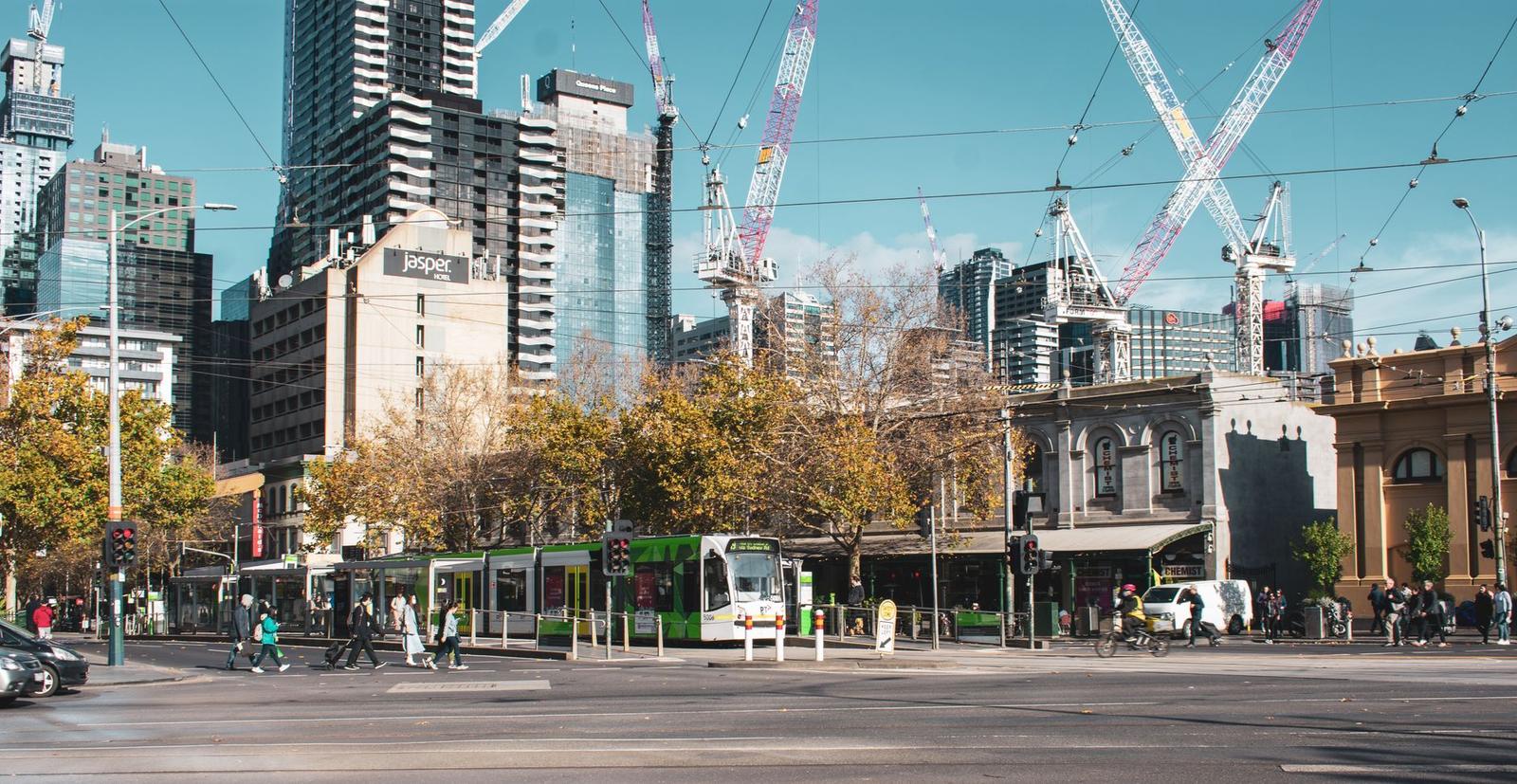 A tram crosses a busy city intersection lined with construction cranes and old buildings