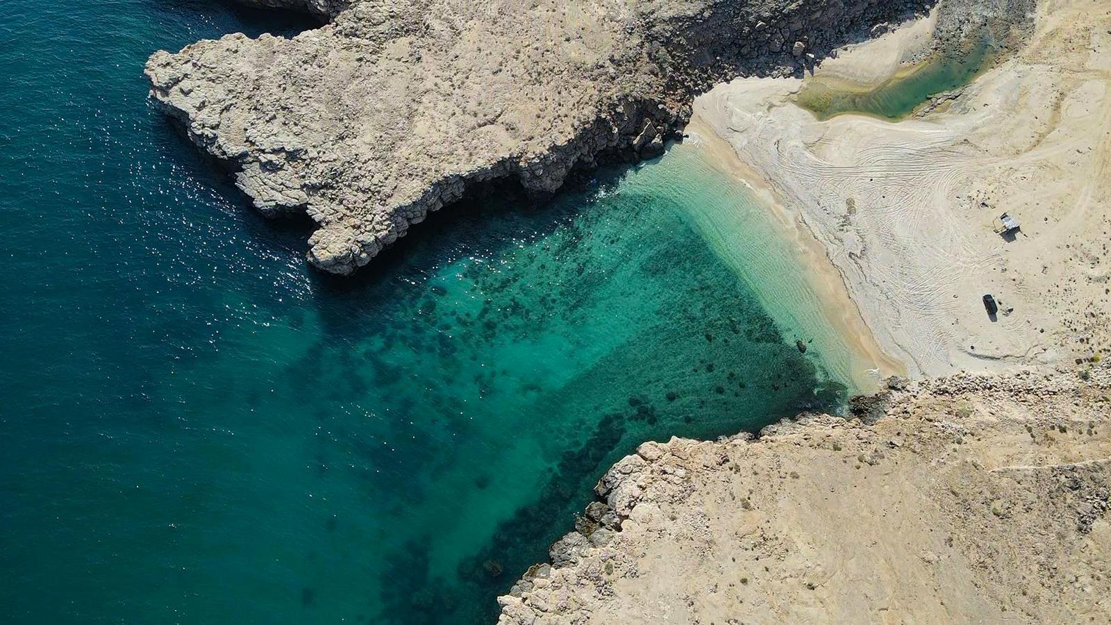 Aerial view of a rocky cove with a small sandy beach and clear water