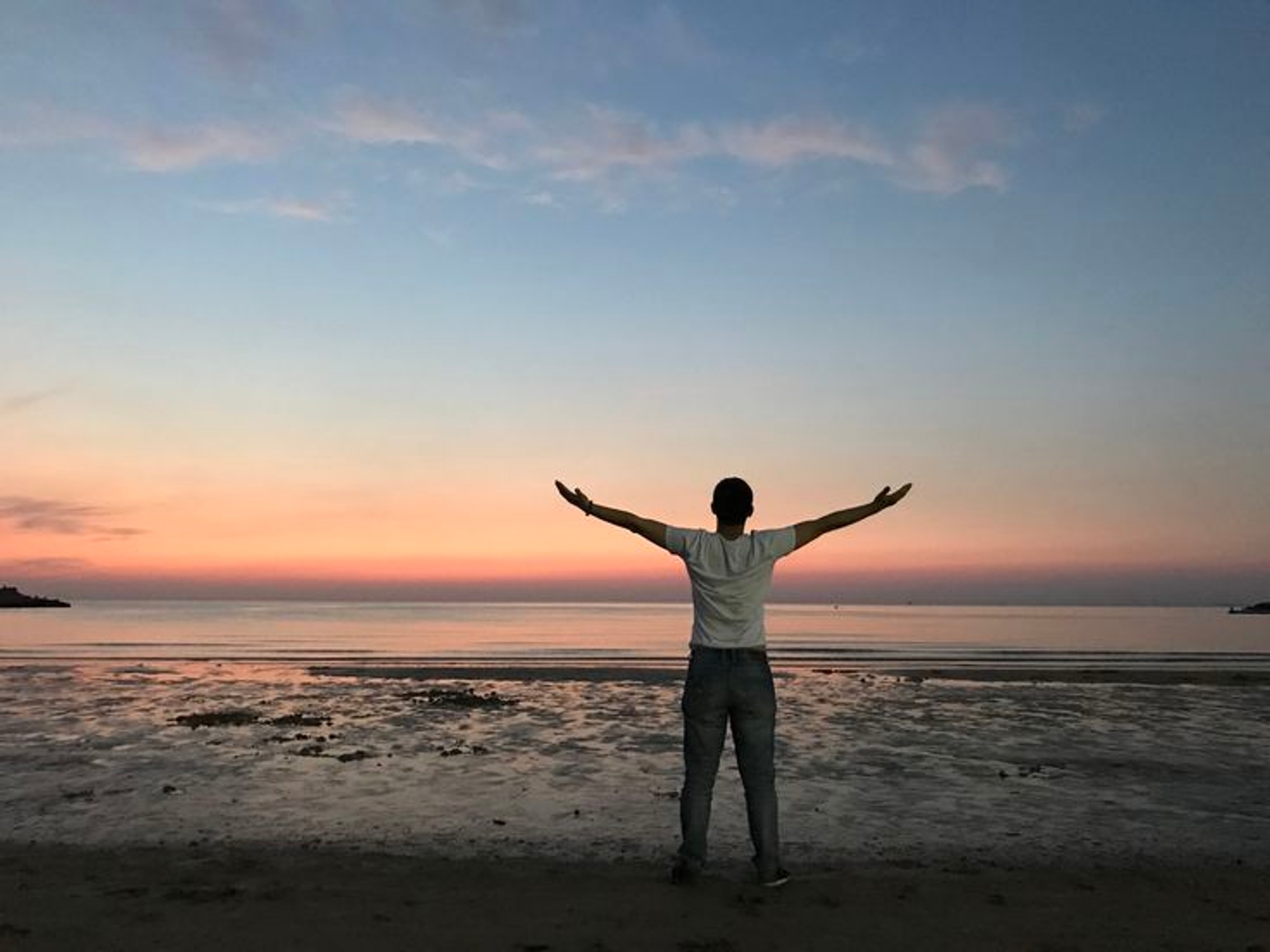 A person standing alone on a wide beach beneath a large cumulus cloud