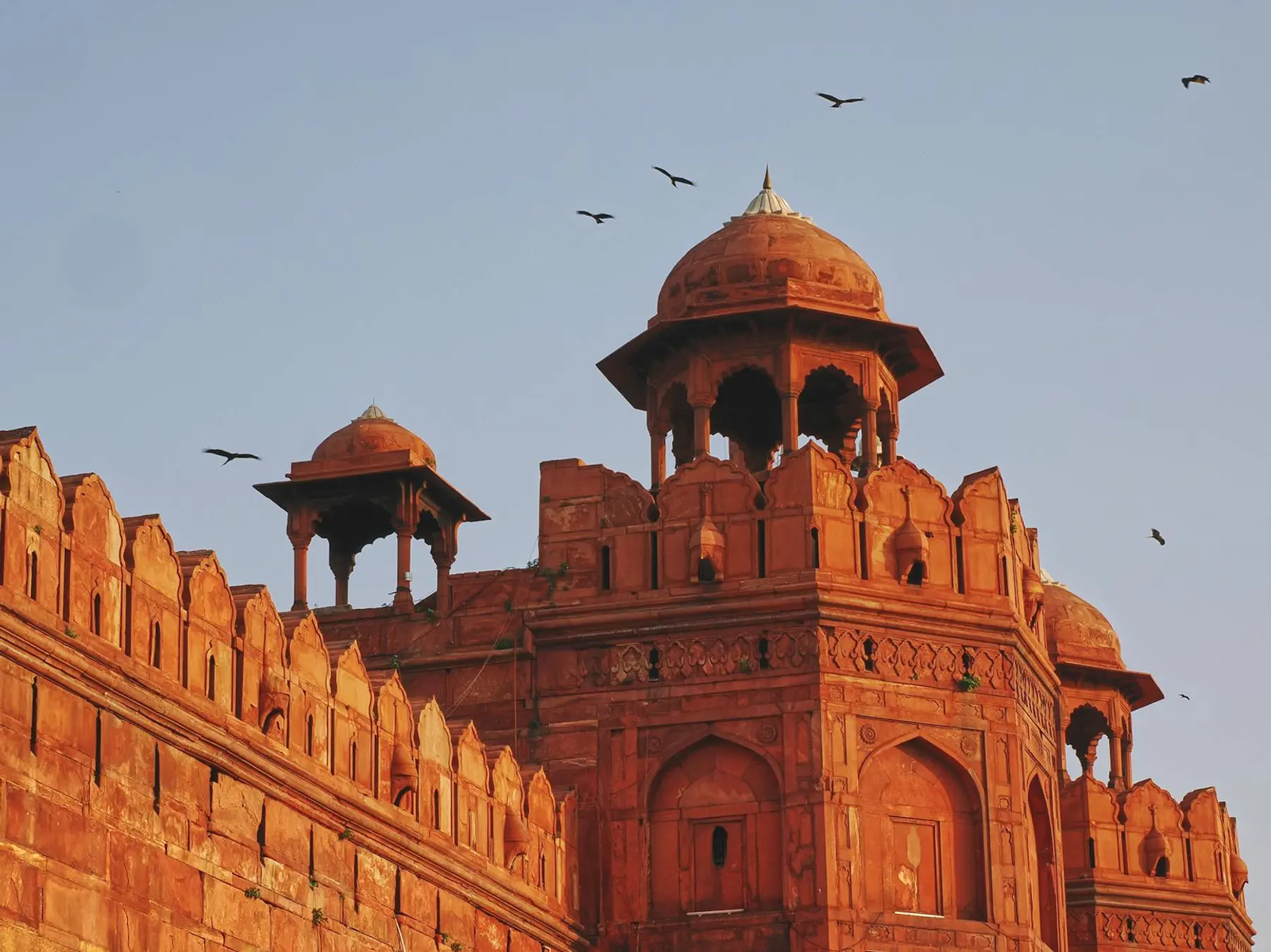 A red sandstone fort tower with domed pavilions and birds circling
