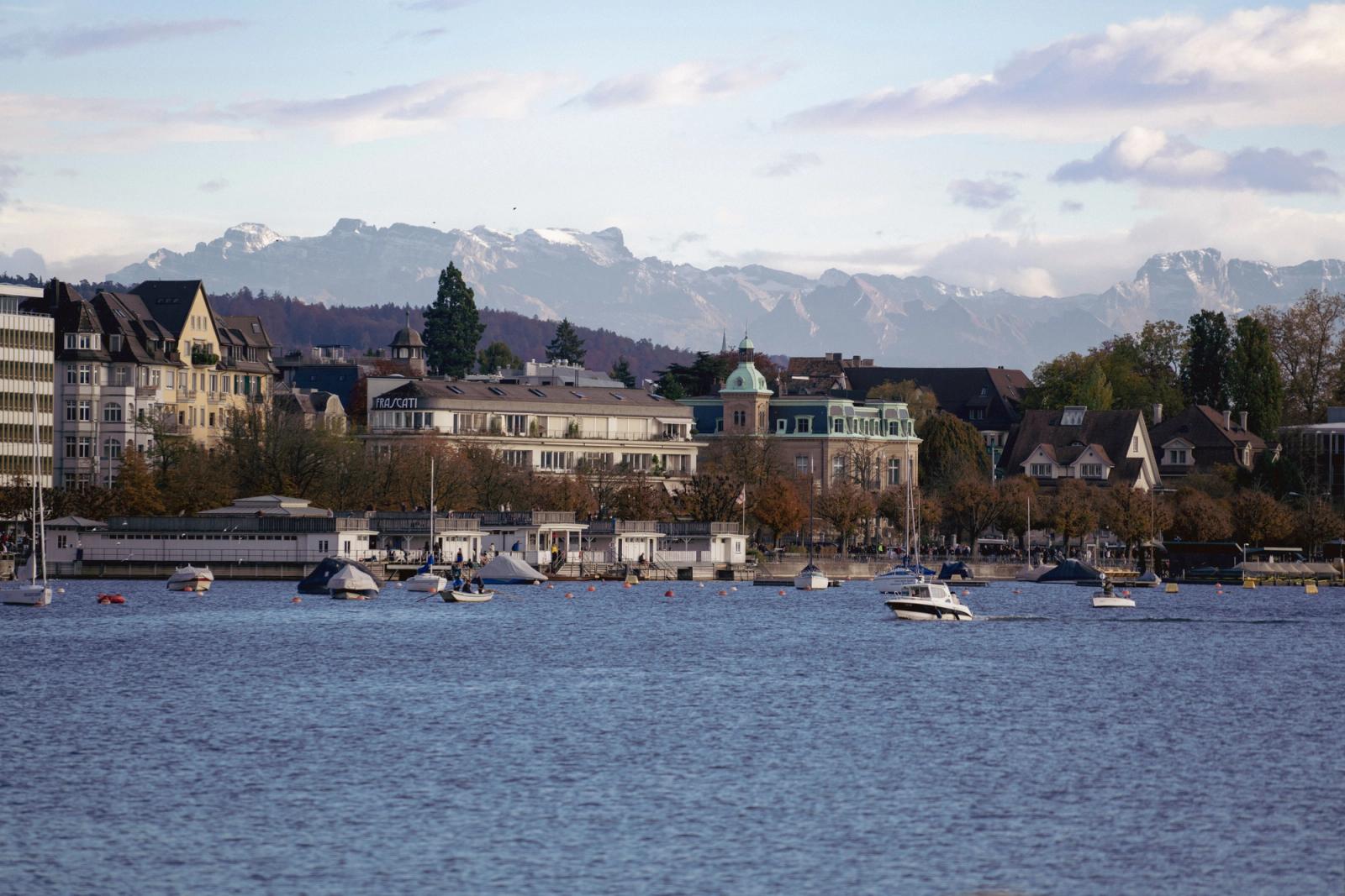 Beautiful waterfront view in Zurich with mountain backdrop and boats on the lake