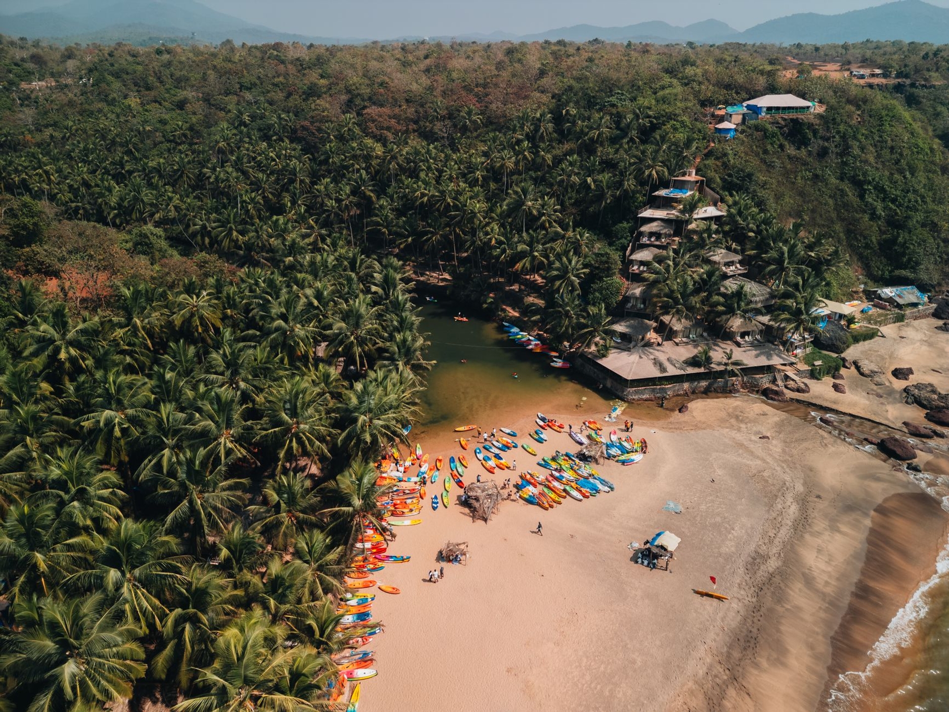 Aerial view of colourful kayaks lined on a palm-fringed beach cove