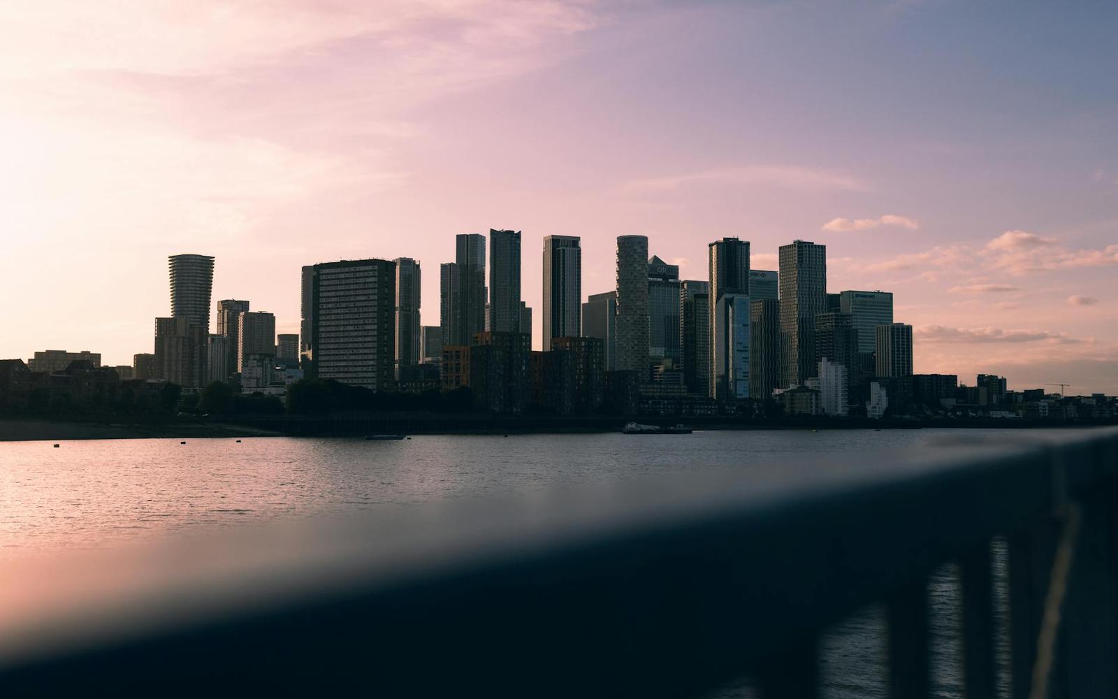 A waterfront city skyline silhouetted against a pastel sunset