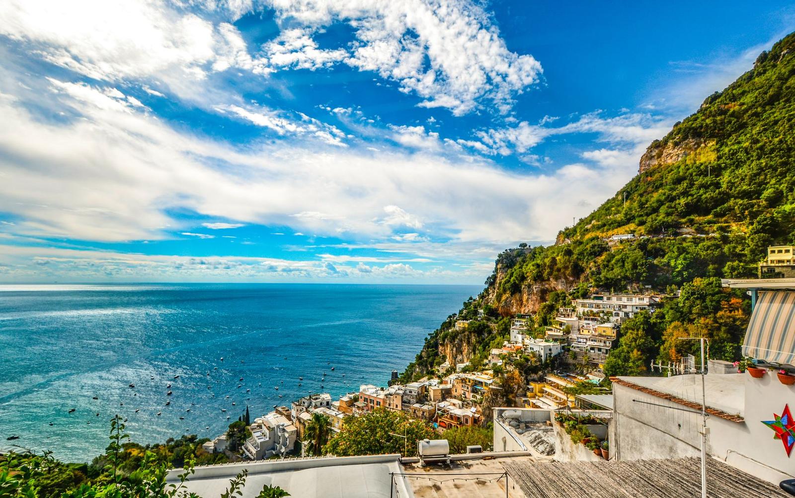 Cliffside coastal town overlooking a wide blue sea under scattered clouds