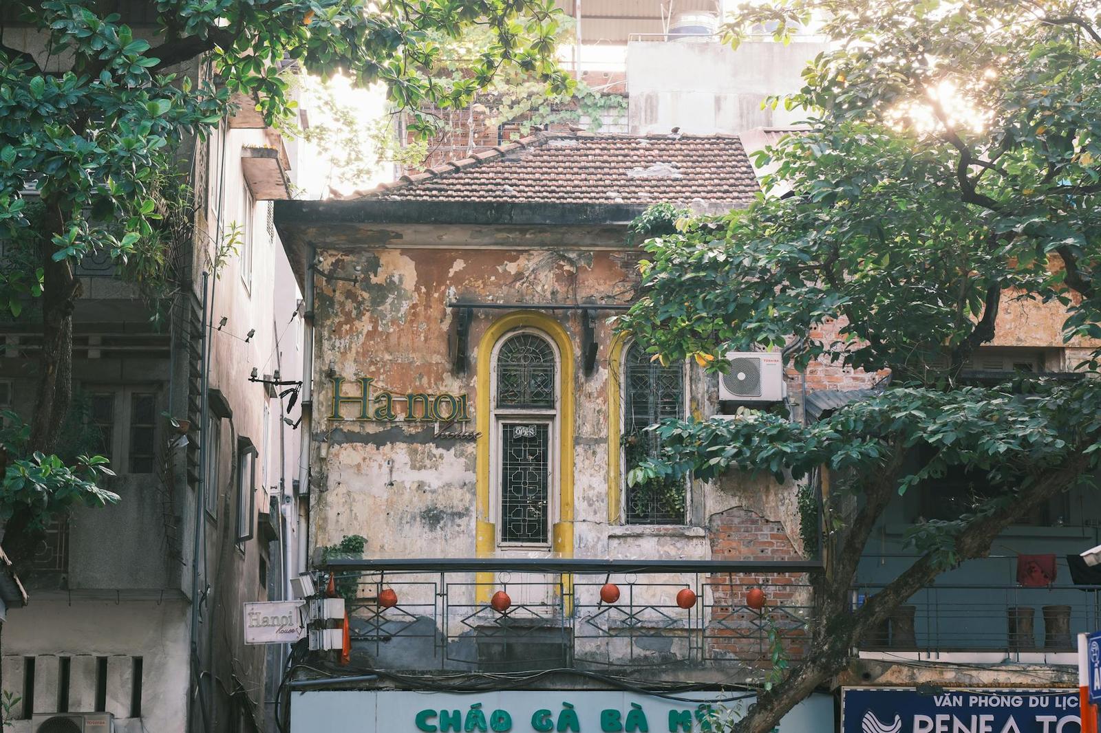 Weathered colonial-era shophouse with wrought-iron balcony under street trees