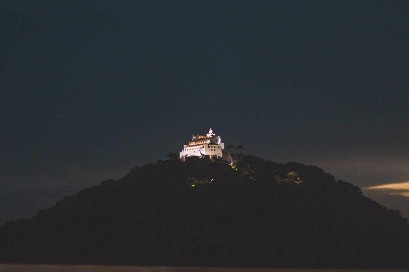 A hilltop temple glowing gold at dusk above a darkened forested hill