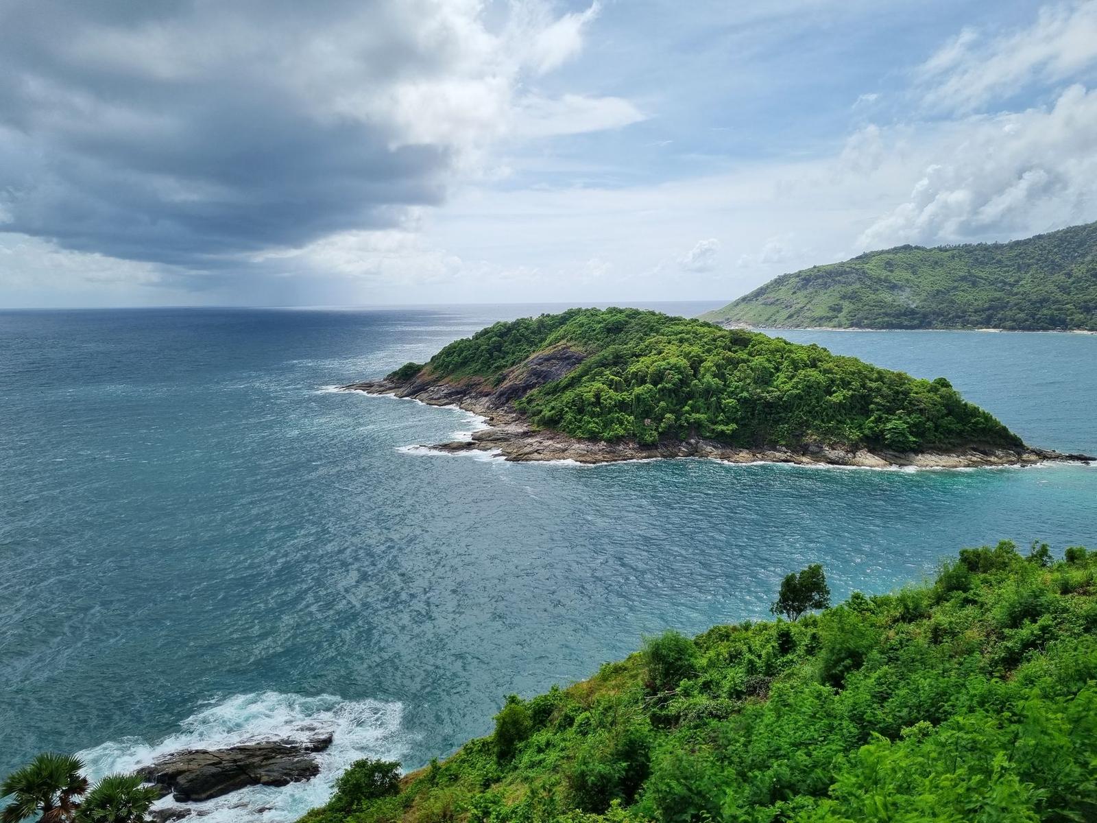Forested headland jutting into the sea beneath a partly cloudy sky