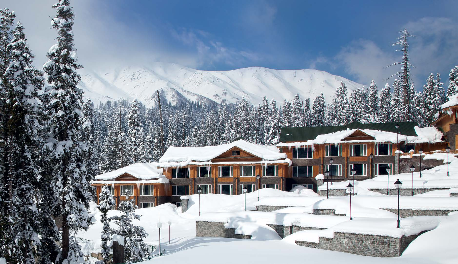 Snow-covered timber chalets set among pine trees below a mountain range