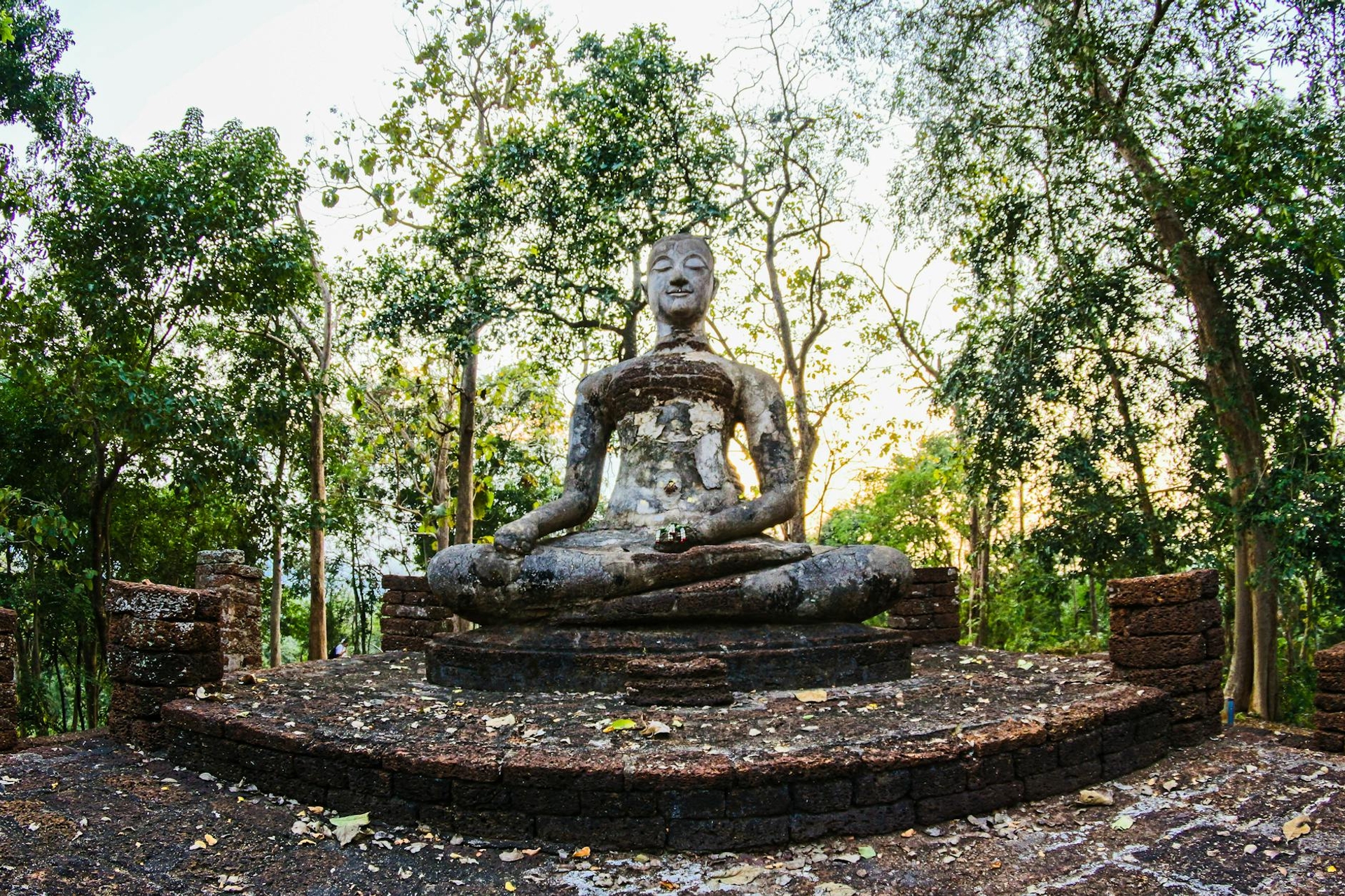 A weathered stone Buddha statue seated in a forest clearing