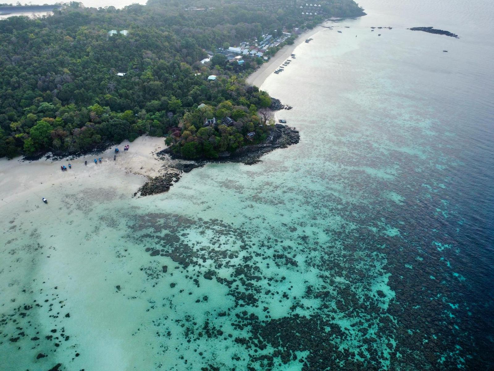 Aerial view of a reef-fringed beach where pale shallows meet deep blue sea