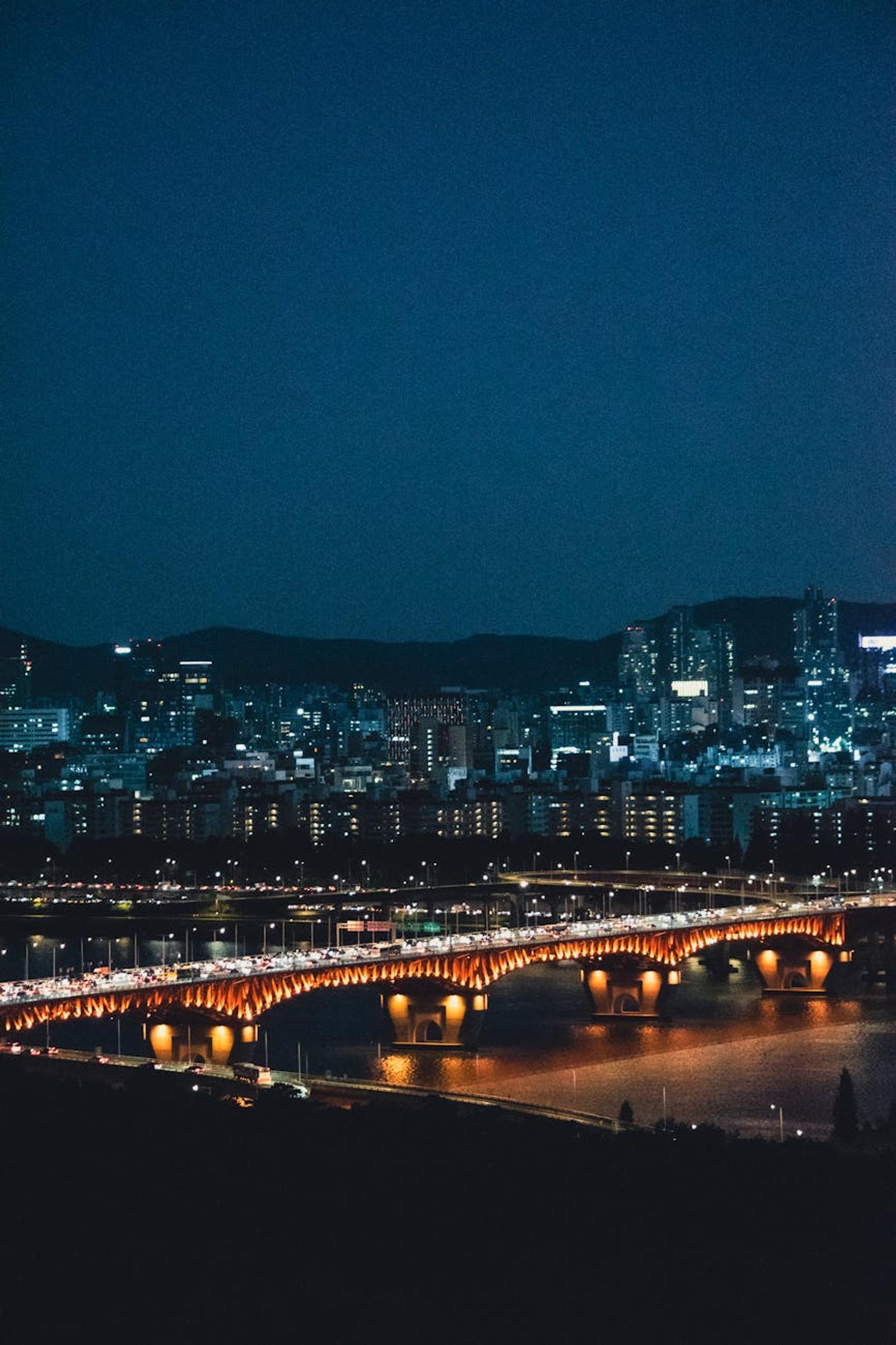 Illuminated bridge crossing a river before a night skyline