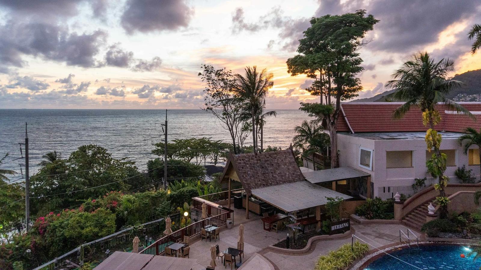 A hotel terrace with a pool and thatched pavilion overlooking the sea at dusk