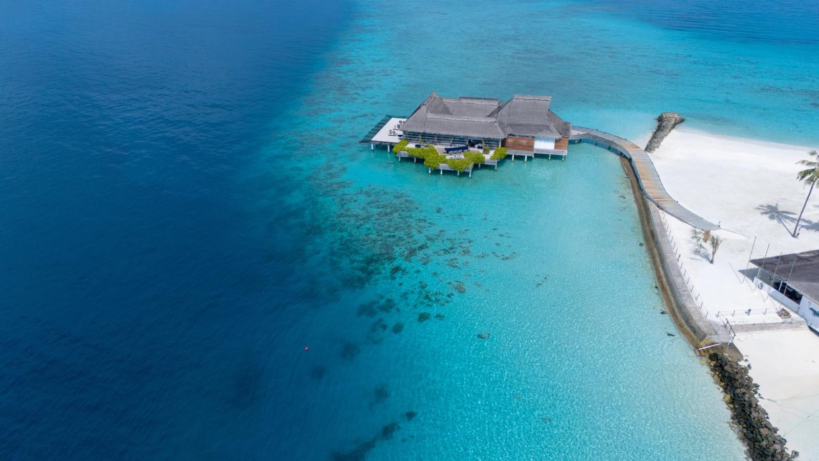 A thatched overwater villa surrounded by clear turquoise reef water
