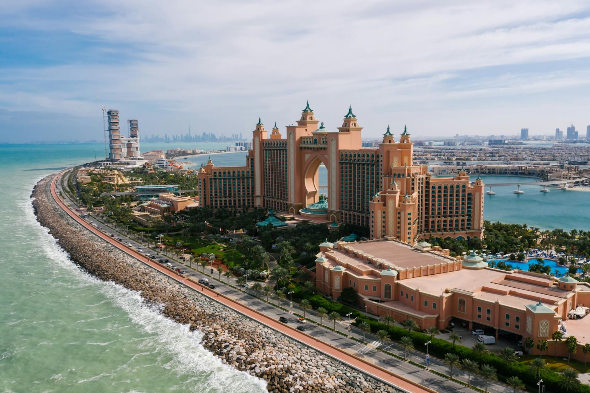 Aerial view of a grand pink hotel complex on a curving palm-shaped shoreline