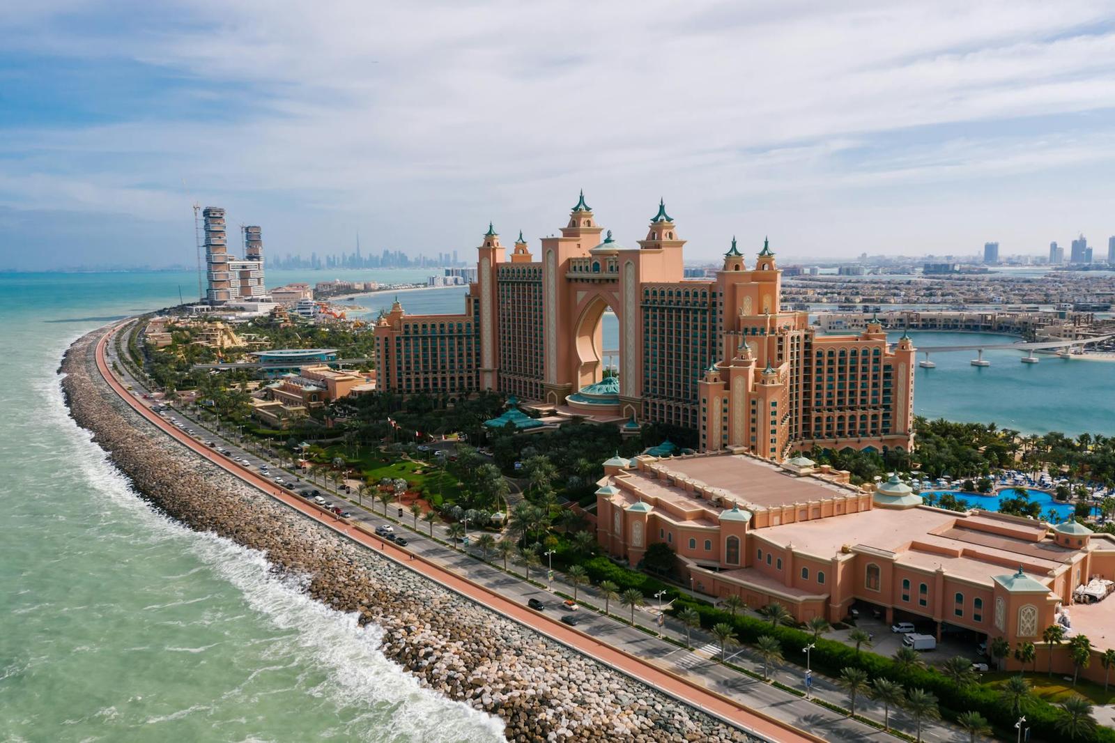 Aerial view of a grand pink hotel complex on a curving palm-shaped shoreline