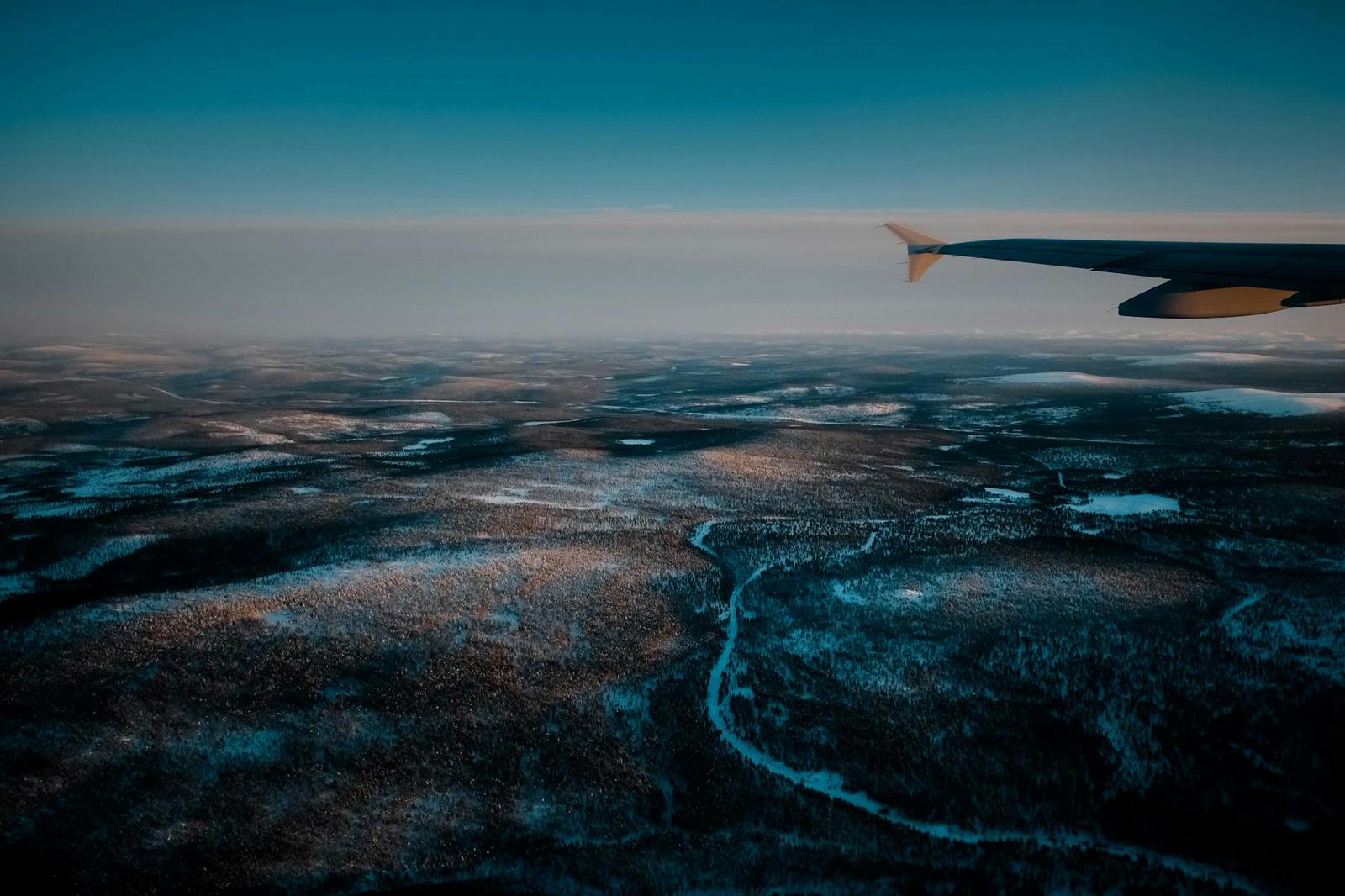 An aerial view of a frozen river winding through snowy tundra from a plane window