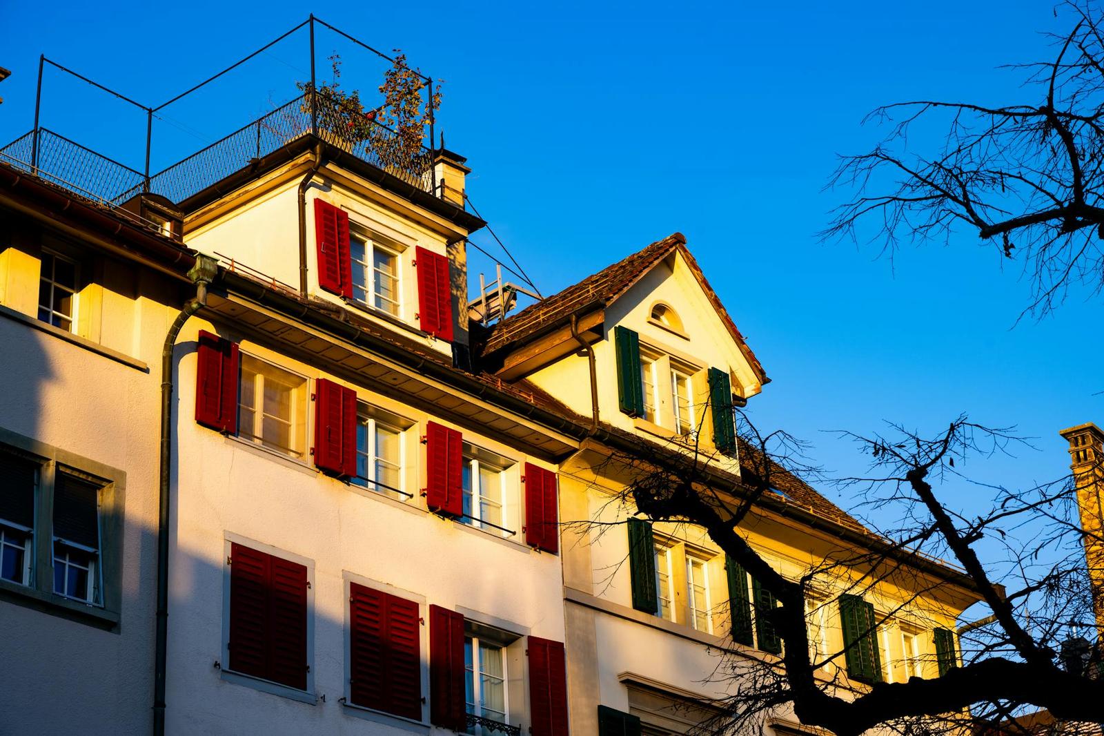 Red-shuttered townhouse facade glowing in warm evening light against a blue sky