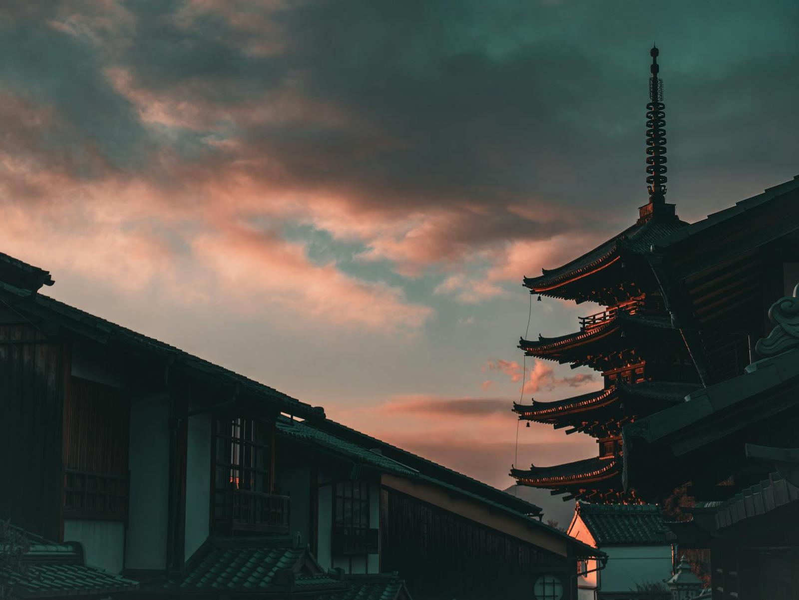 A pagoda silhouette against a pink sunset sky above traditional rooftops