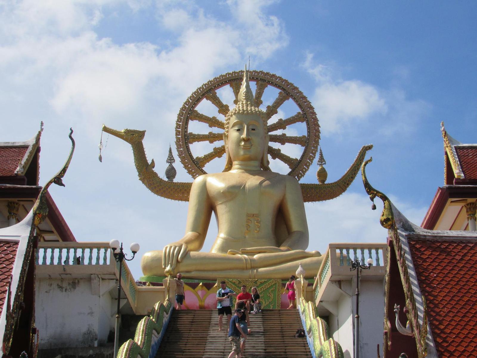 Golden seated Buddha statue towering above a hilltop temple