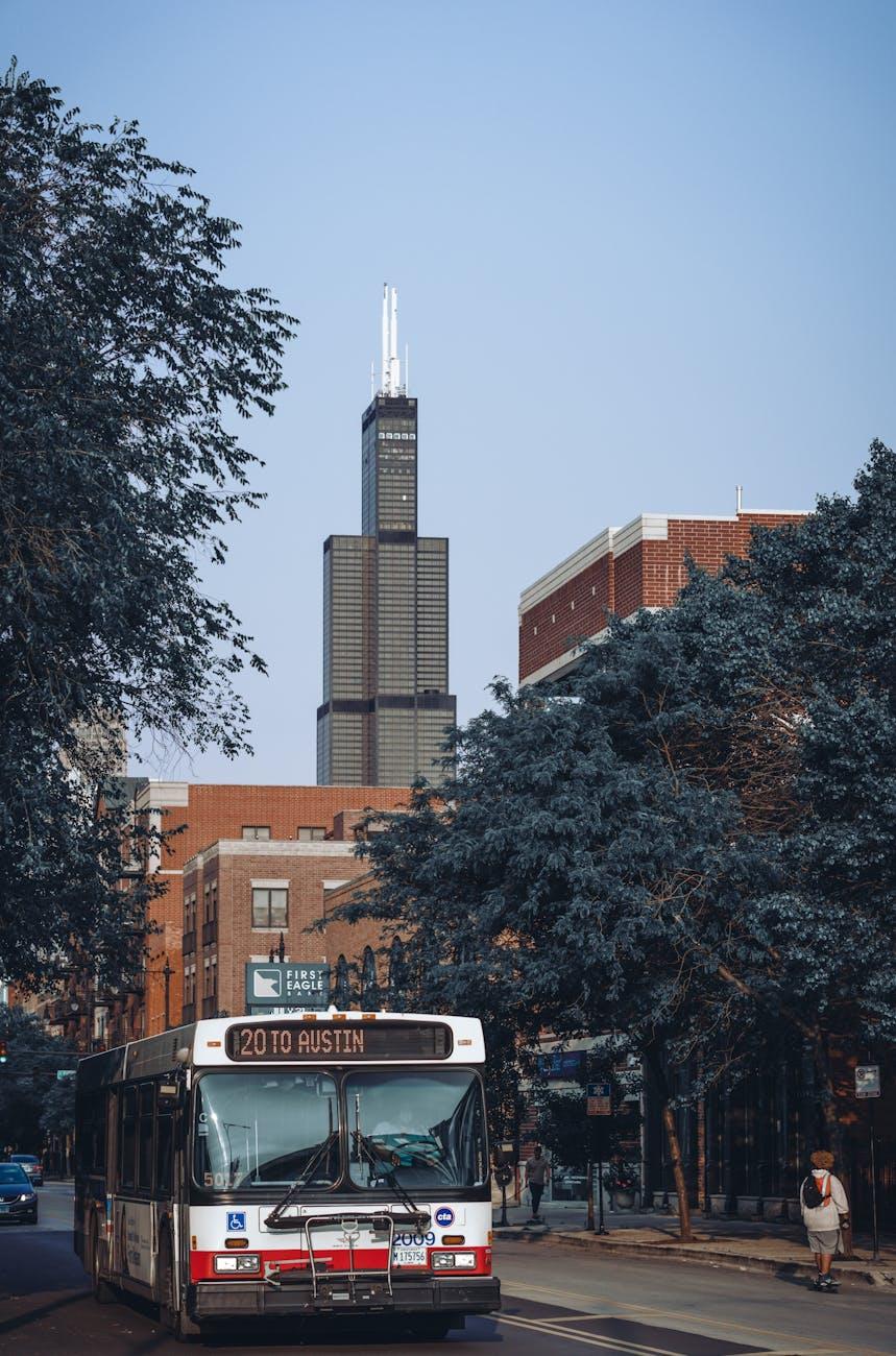 City bus on a tree-lined street below a tall black skyscraper