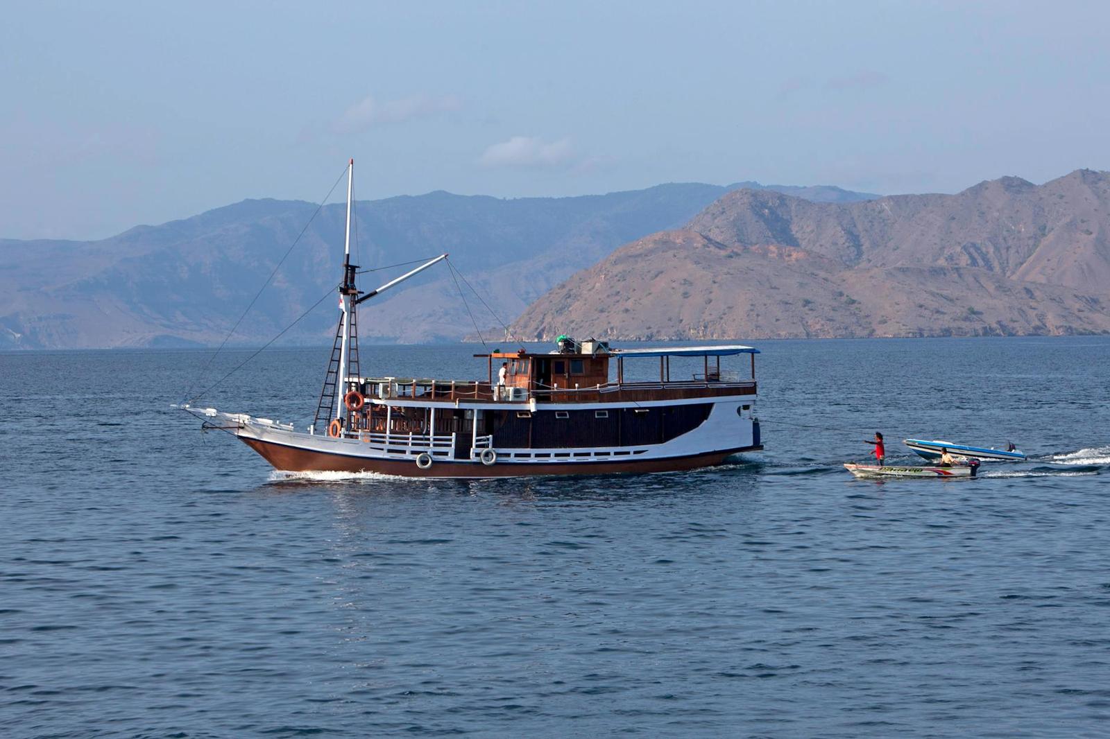 A wooden sailing boat drifts on calm water near rugged hills