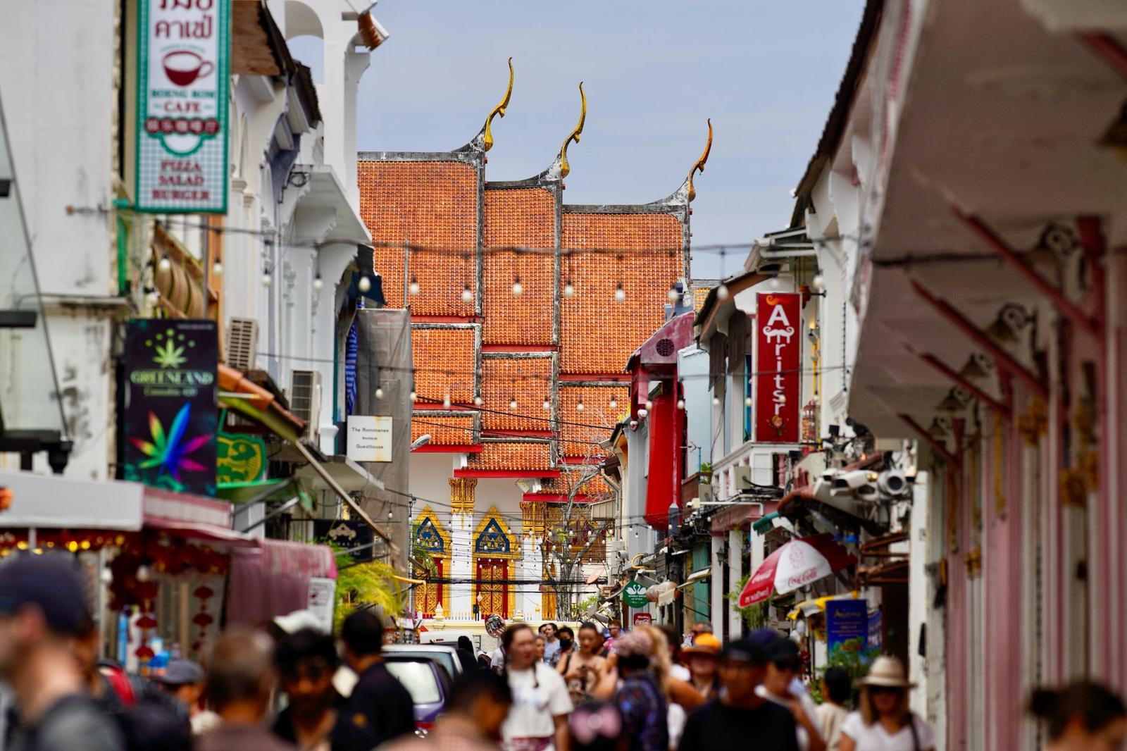 Crowded pedestrian street with a temple roofline and hanging signs