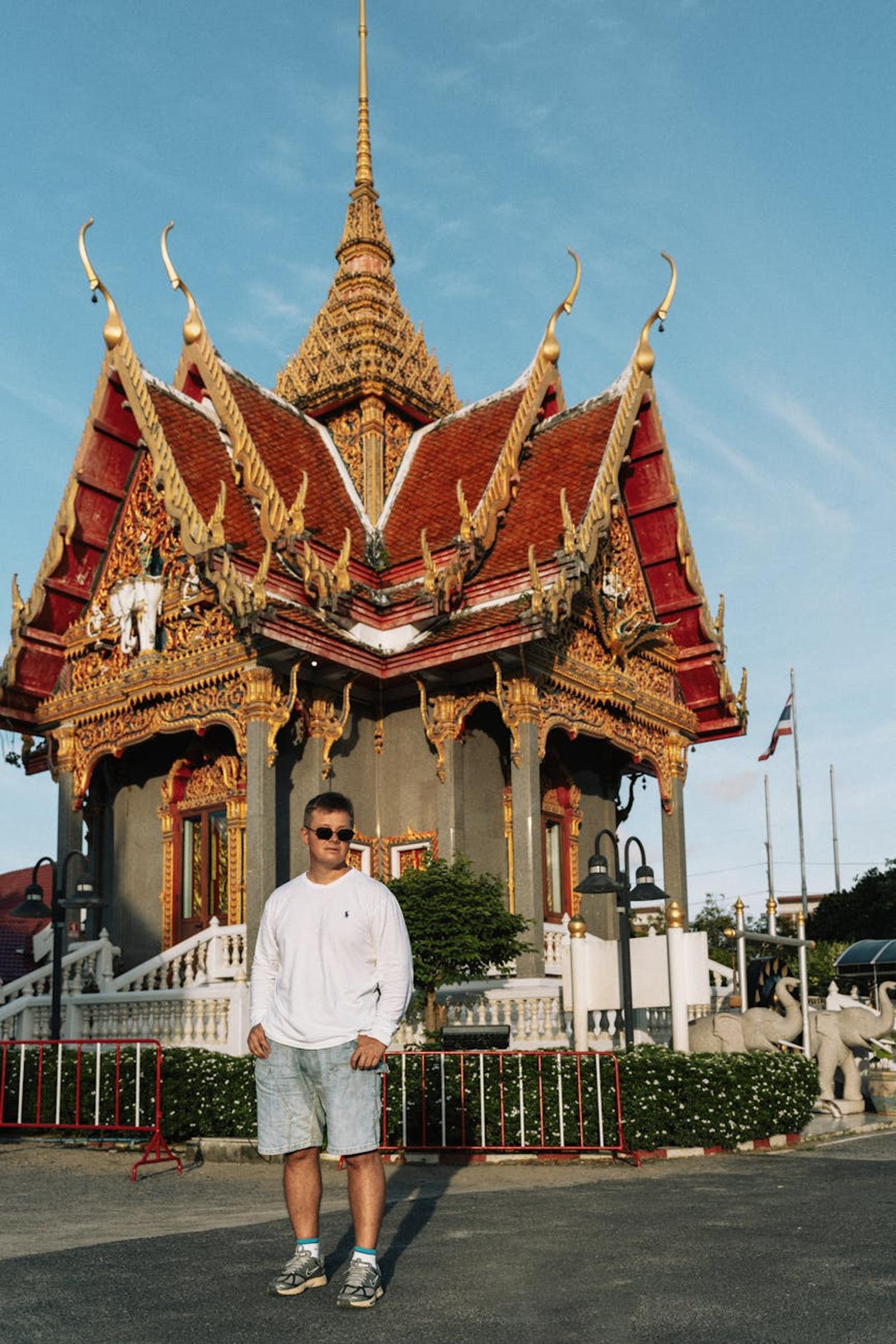 Man standing before an ornate red and gold temple pavilion