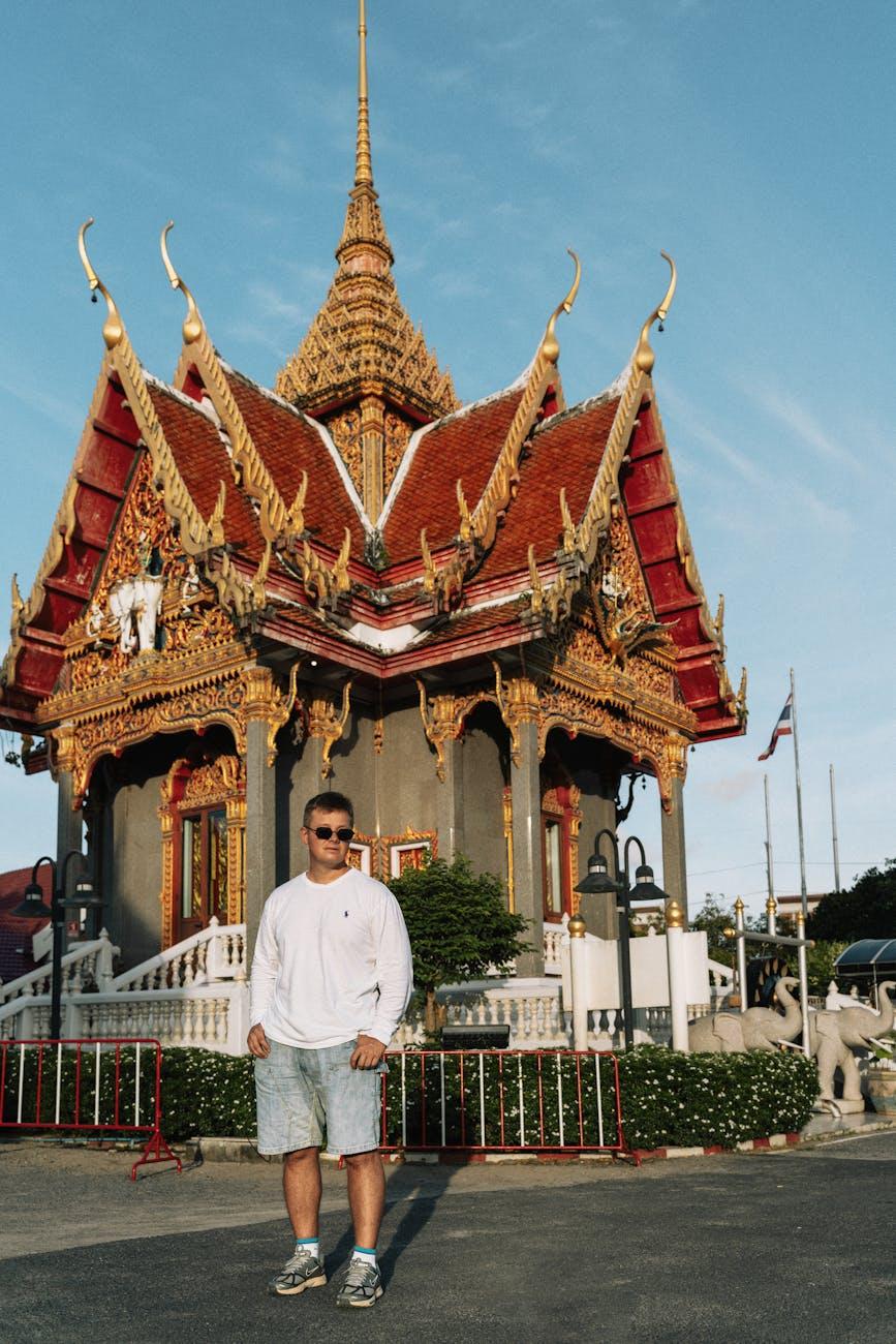 Man standing before an ornate red and gold temple pavilion